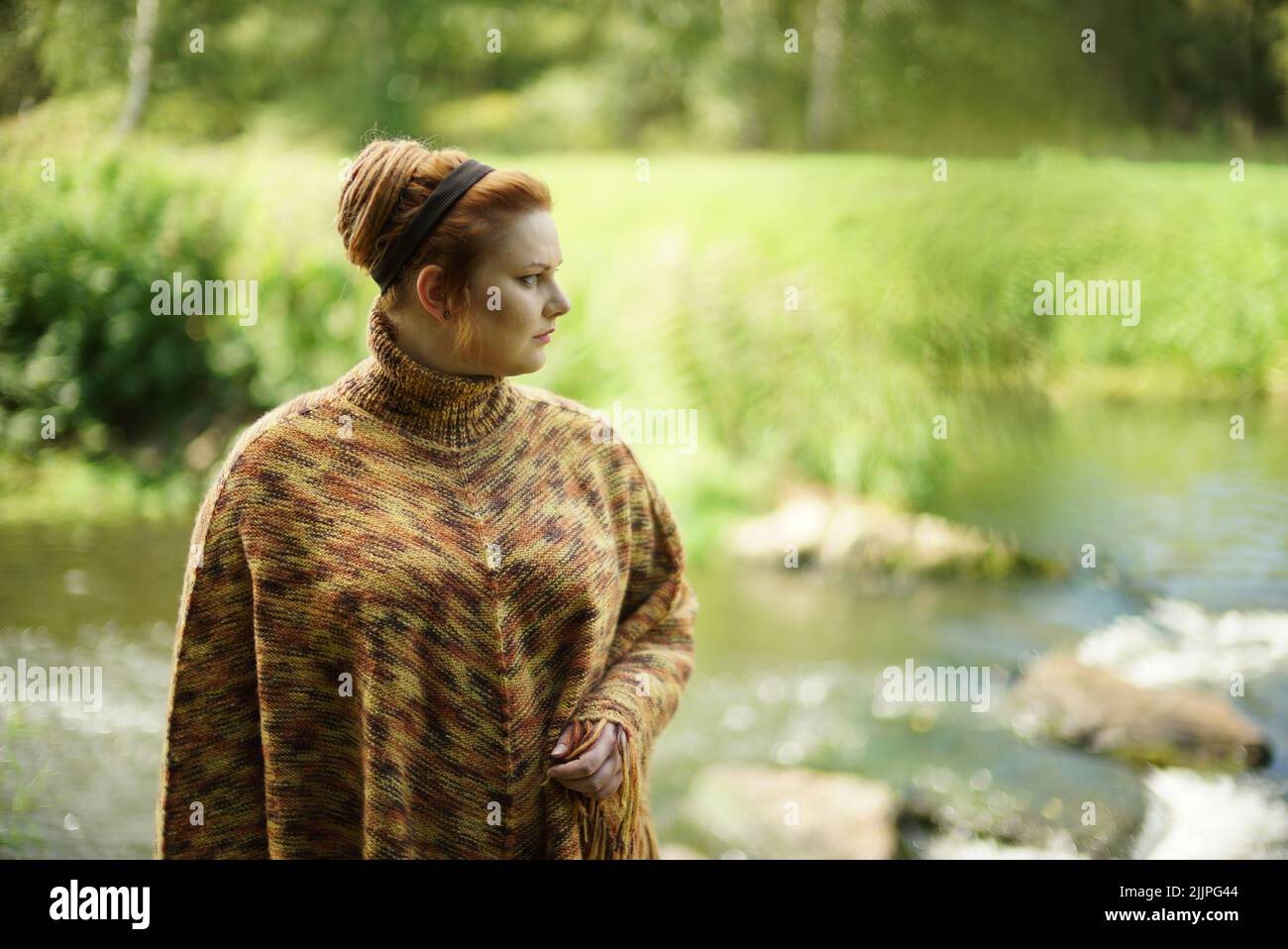 Une femelle blanche et chubby avec des cheveux de gingembre dans un petit pain se posant près d'une rive de rivière Banque D'Images
