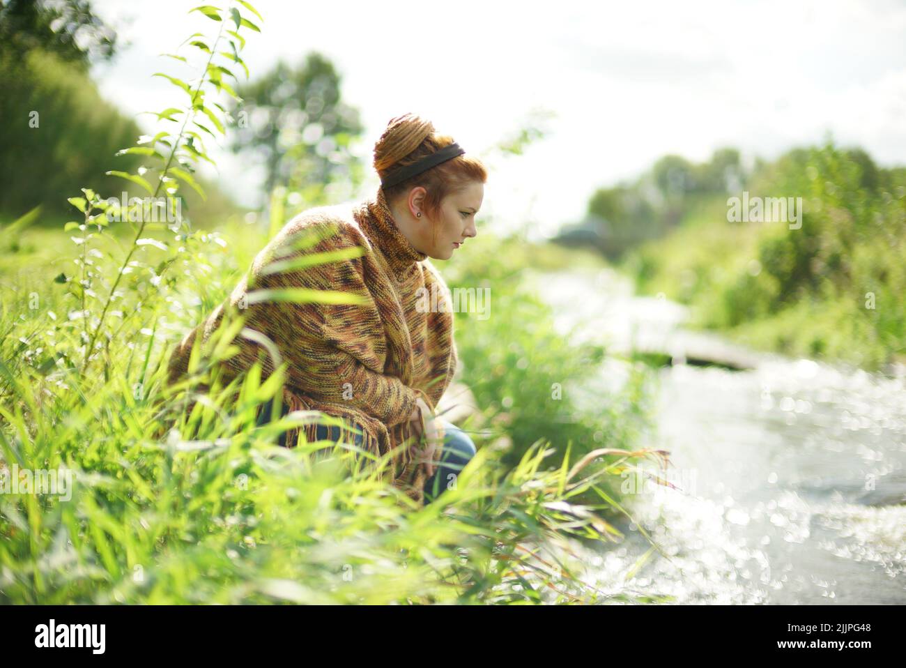 Une femelle blanche et chubby aux cheveux de gingembre dans un petit pain qui regarde une rivière depuis le rivage Banque D'Images