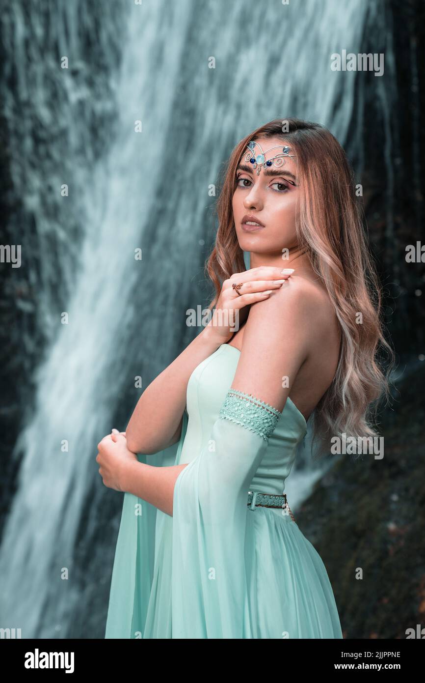 Un cliché vertical d'une jeune femme dans une robe verte et des bijoux sur le front se posant près d'une chute d'eau Banque D'Images