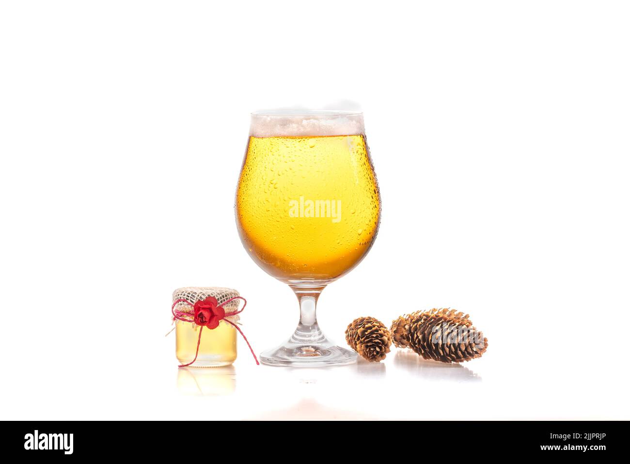 Un gros plan d'un verre de bière au miel léger, un petit pot de miel et quelques cônes isolés sur un fond blanc Banque D'Images
