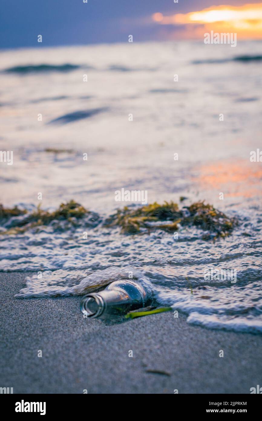 Un plan vertical d'une bouteille sur la plage de sable au coucher du soleil - pollution concept Banque D'Images