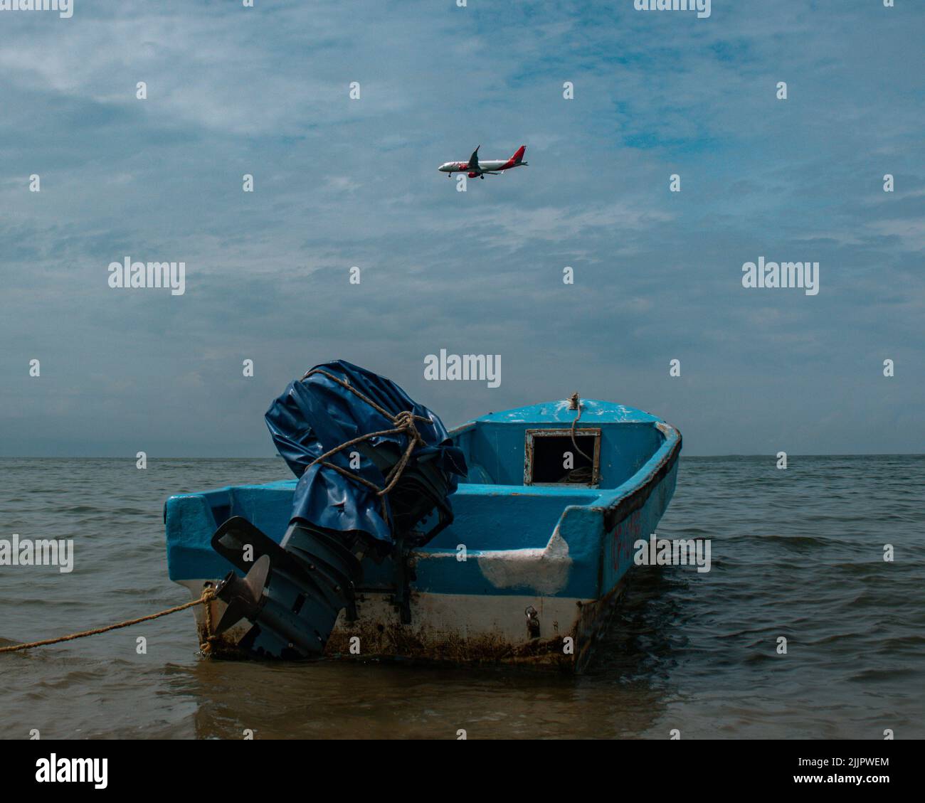 Gros plan d'un vieux bateau bleu flottant en mer avec un avion volant dans le ciel Banque D'Images Gros plan d'un vieux bateau bleu flottant en mer avec un avion volant dans le ciel Banque D'Images