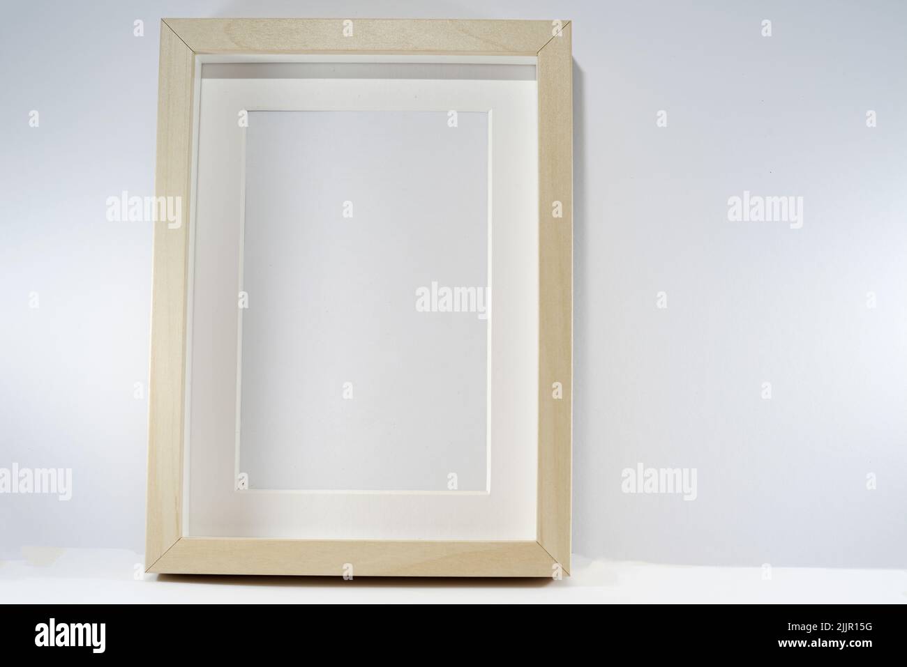 Un gros plan d'un cadre photo en bois vide sur un fond blanc Uni appuyé sur un mur Banque D'Images
