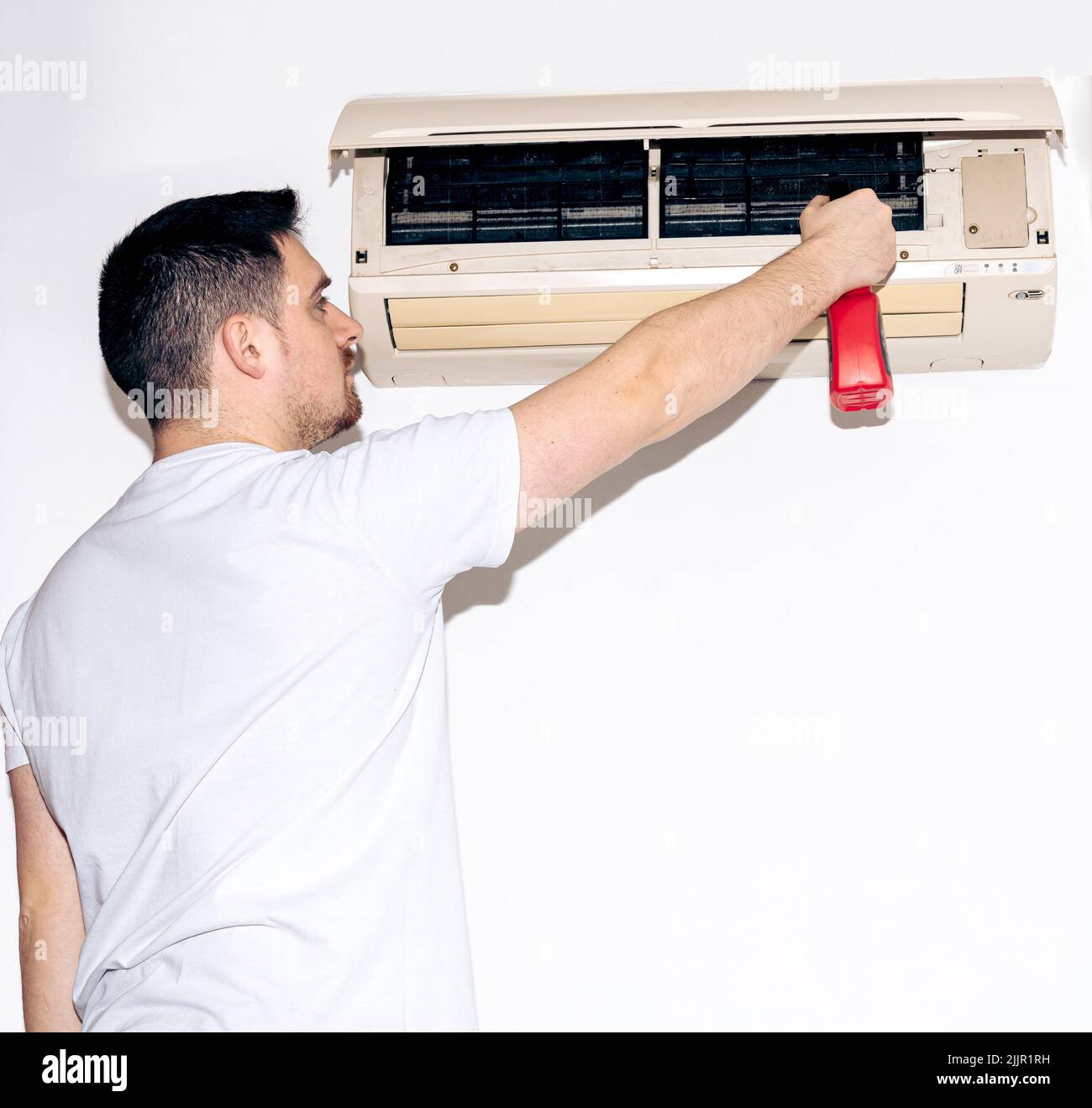 Homme caucasien tenant un pulvérisateur pour nettoyer le climatiseur sur un mur blanc Banque D'Images