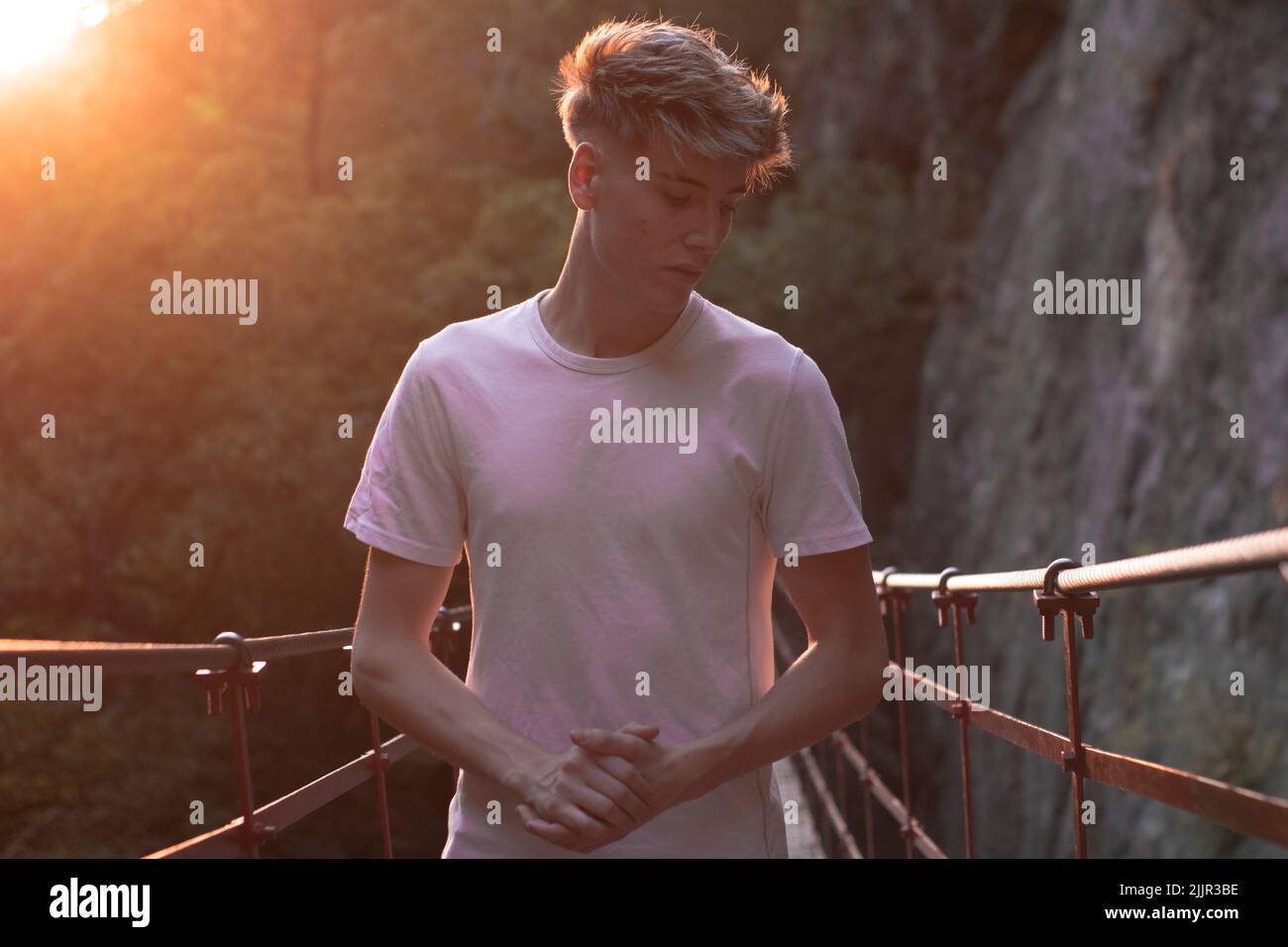 Un petit foyer d'un jeune et beau mâle caucasien posant sur un pont dans un parc contre les rayons du soleil Banque D'Images