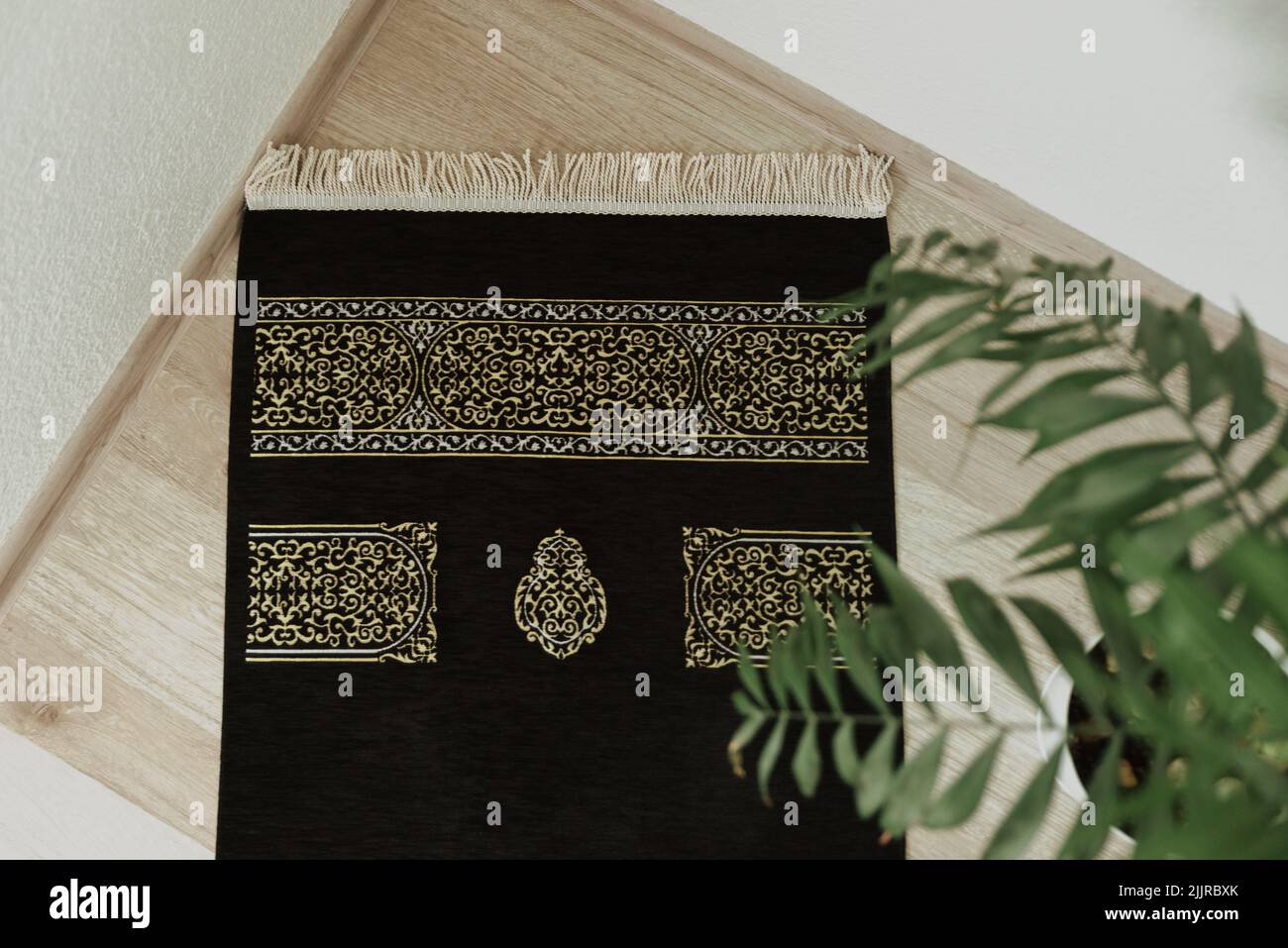 Une vue de dessus d'un tapis de prière en velours noir avec un motif Kaaba dans le coin sur un fond d'une plante de maison Banque D'Images