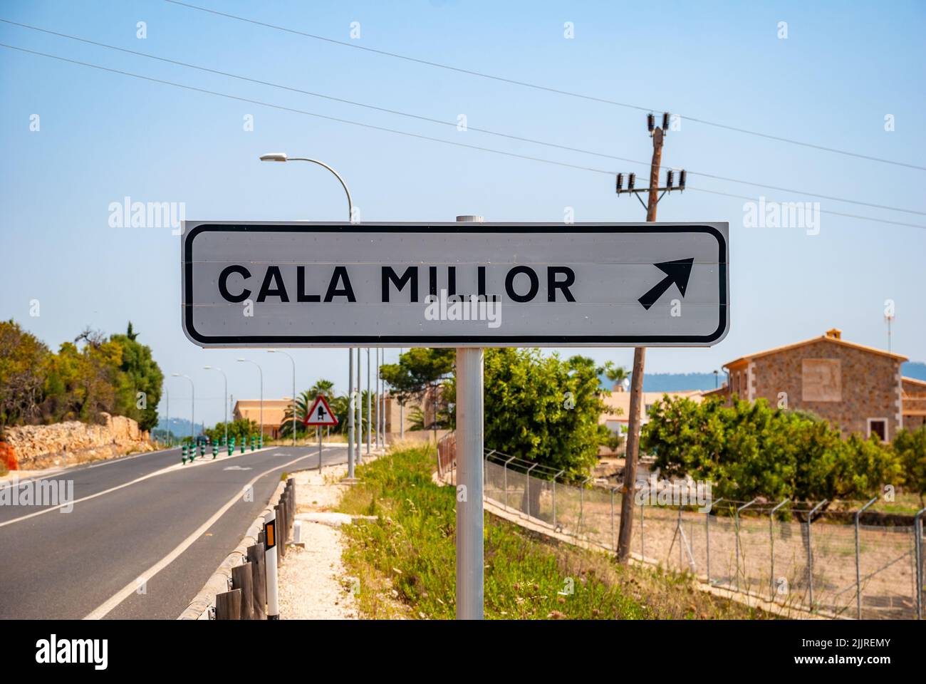 Un panneau indiquant la direction de Cala Millor sur le bord de la route avec des buuldings Banque D'Images