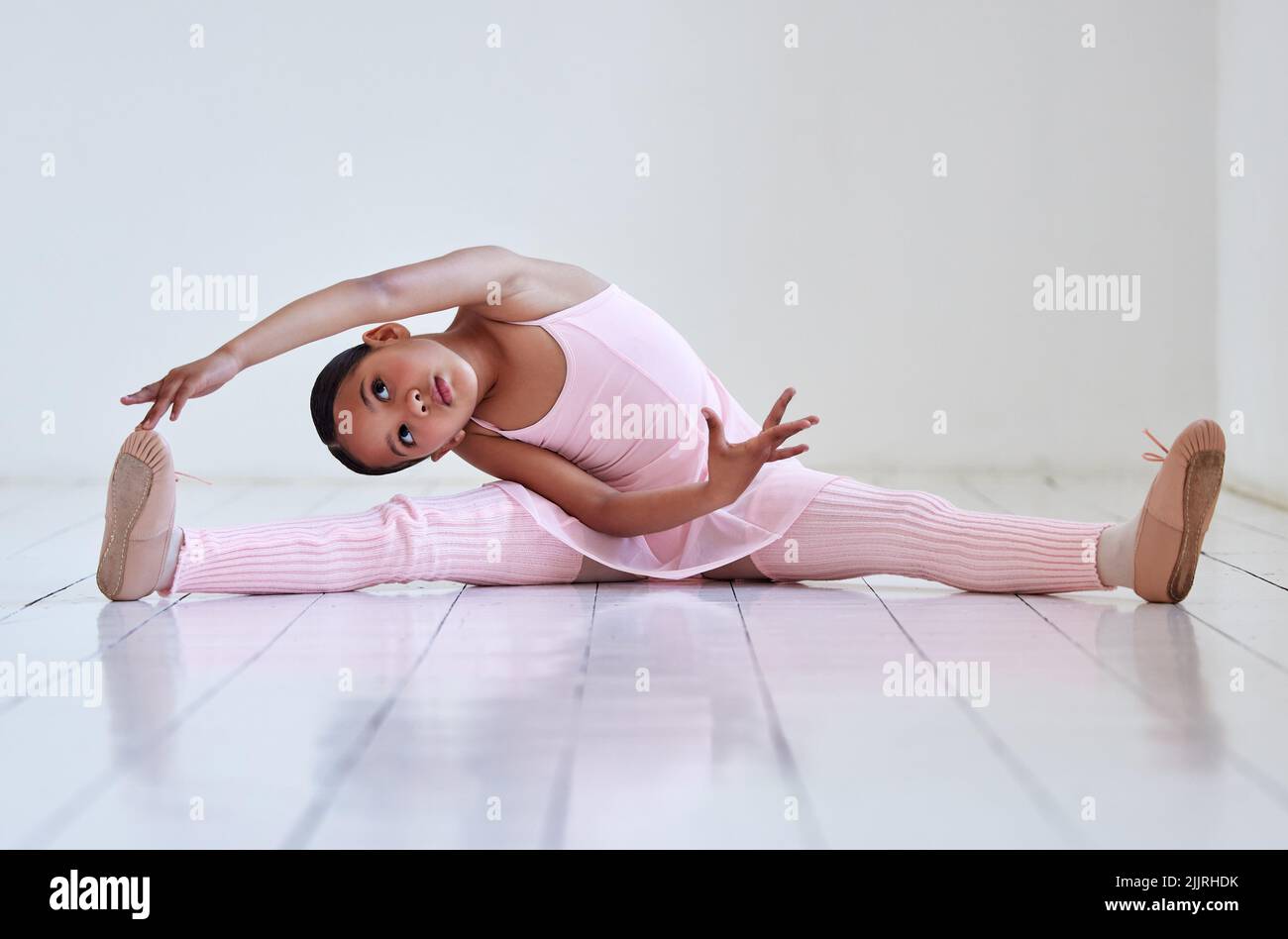 Se réchauffer avant de pratiquer sa routine. Une petite fille faisant les fractionnements dans un studio de ballet. Banque D'Images