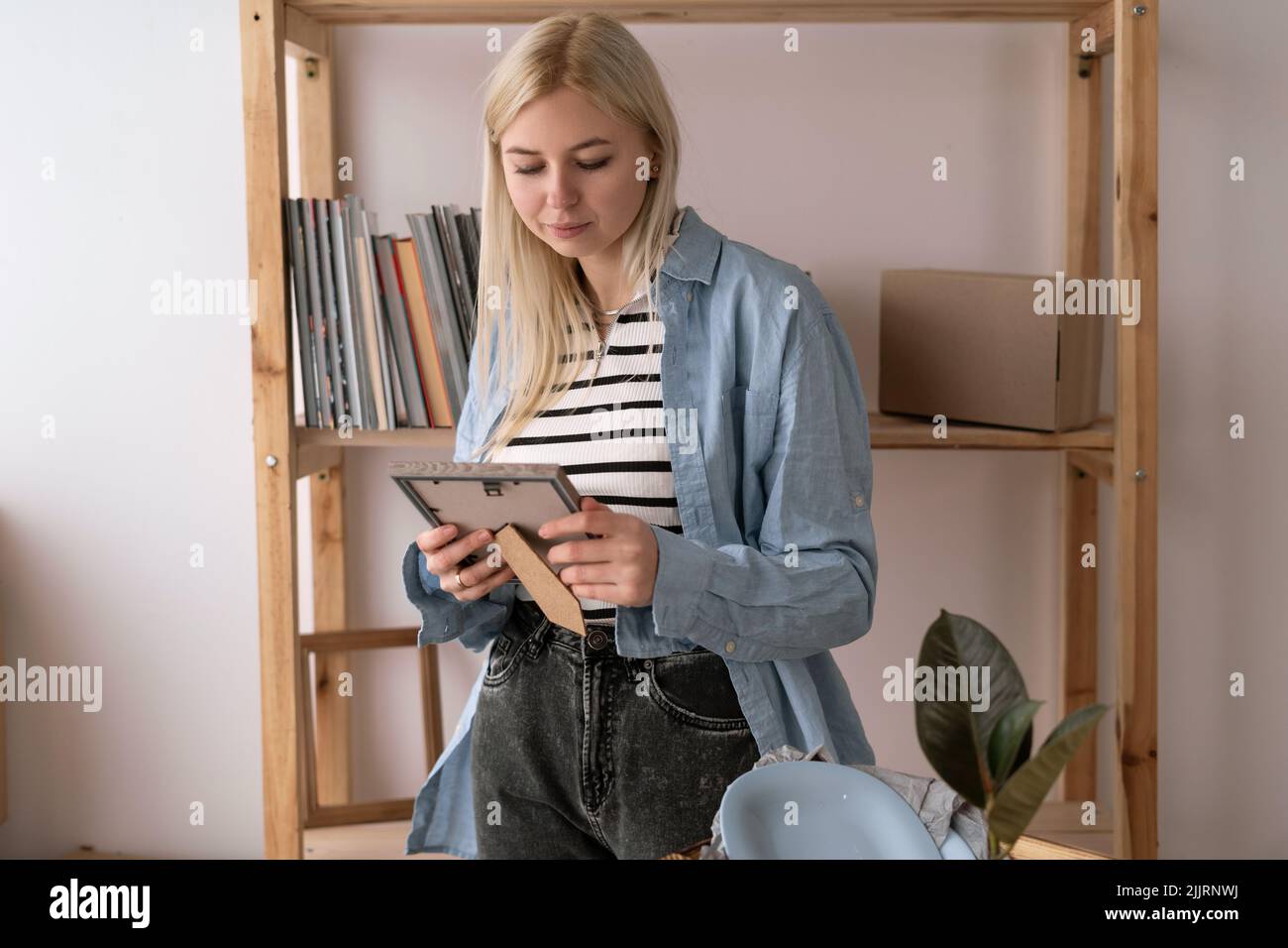 jour de déménagement. Joyeuse fille emballant une photo encadrée dans une grande boîte et souriant largement tout en se préparant à sortir. Mémoire. Banque D'Images