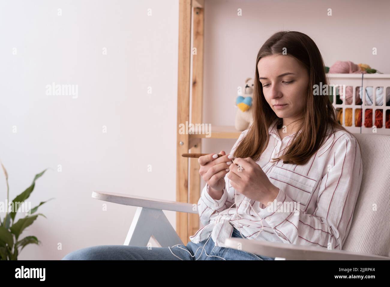 Femme tricots crochet. Fille assise sur le fauteuil et tricotage à partir de fils. Filets épais en crochet. Confort à la maison. Concept de loisir et de passe-temps Banque D'Images