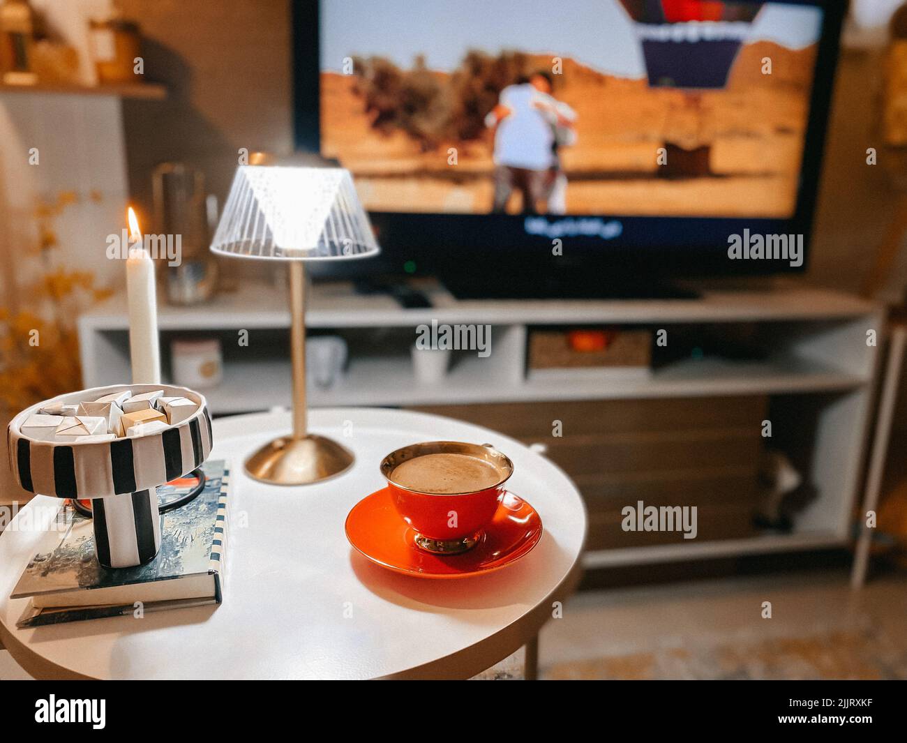 Un gros plan d'une tasse de café magnifiquement arrangé sur une table décorée d'une lampe contre un téléviseur Banque D'Images