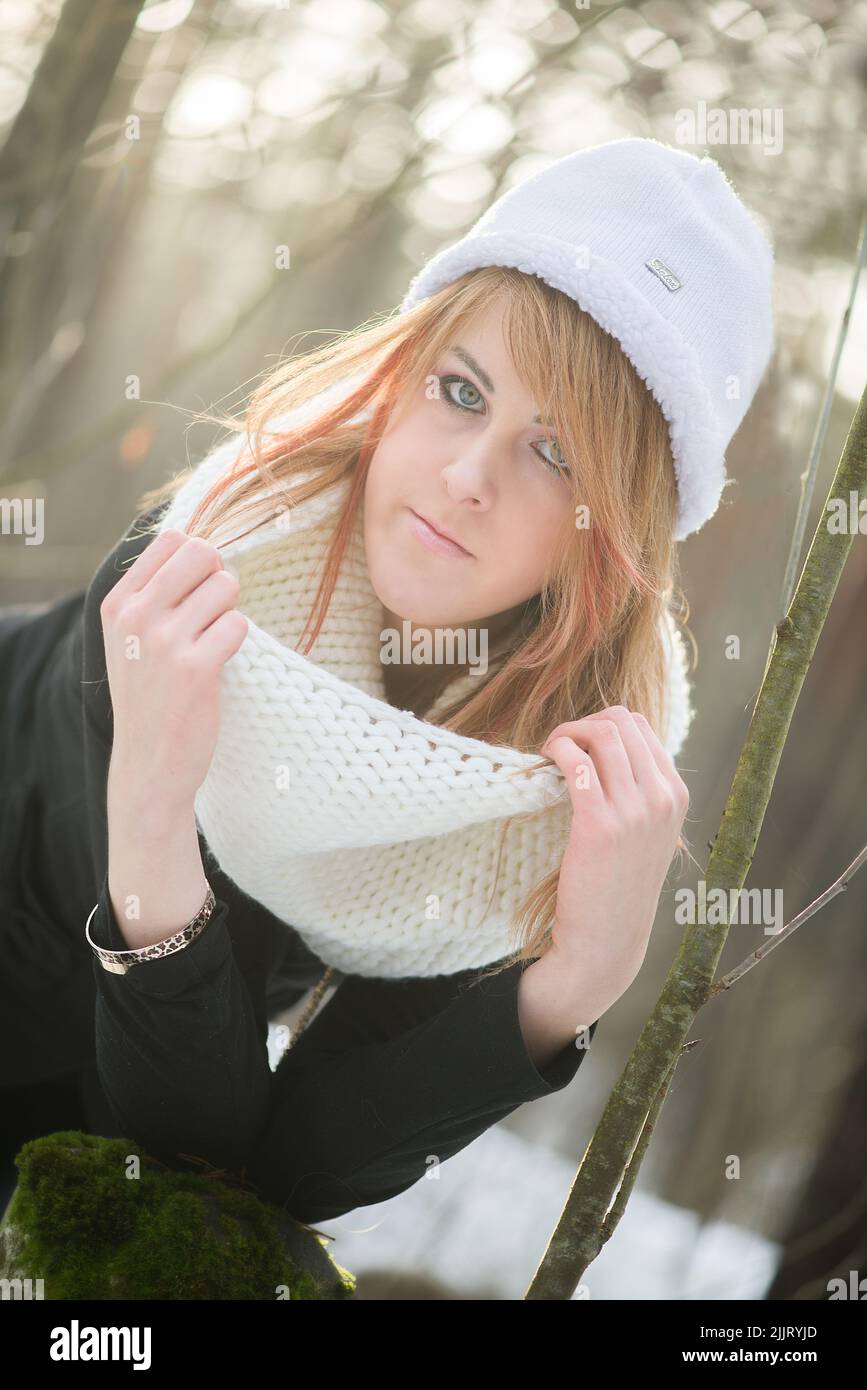 Portrait d'une fille blonde de race blanche portant un chapeau d'hiver blanc avec un fond enneigé flou Banque D'Images