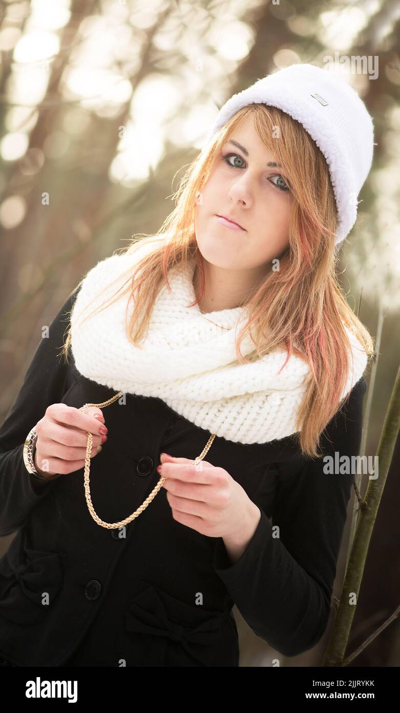 Portrait d'une fille blonde de race blanche portant un chapeau d'hiver blanc avec un fond enneigé flou Banque D'Images