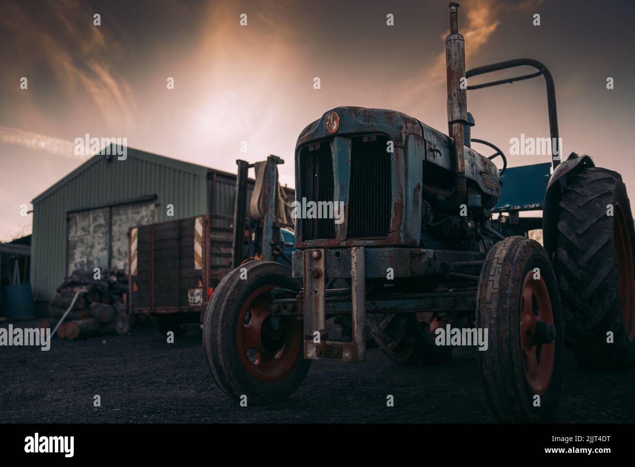 Une photo d'un vieux tracteur rouillé avec un logo dans une ferme sous le ciel illuminé de la soirée Banque D'Images