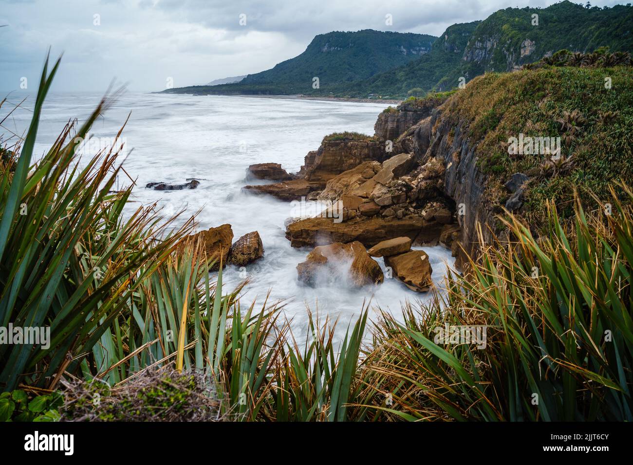 Une vue à couper le souffle depuis le rivage d'eau mousseuse avec des collines en arrière-plan à Pancake Rocks, Westport, Nouvelle-Zélande Banque D'Images