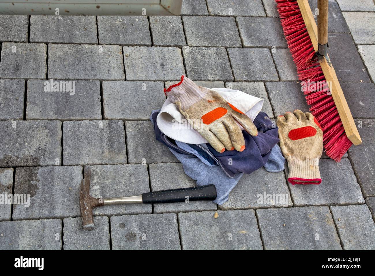 Un marteau, des gants, des T-shirts et un balai sur des dalles de chaussée en béton récemment posées Banque D'Images