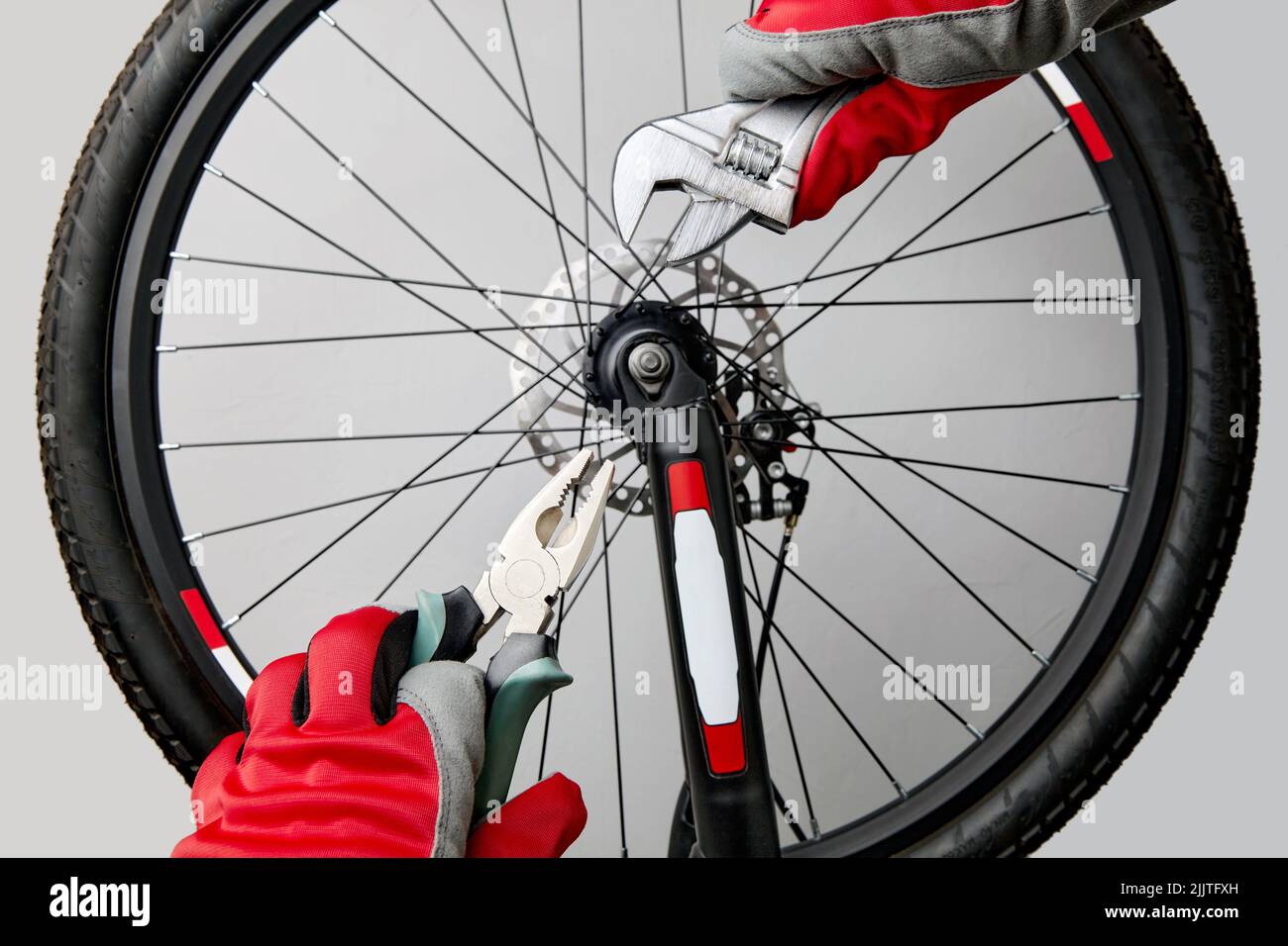 Mains dans des gants de protection avec des clés réglables et des pinces sur l'arrière-plan d'une roue de vélo Banque D'Images