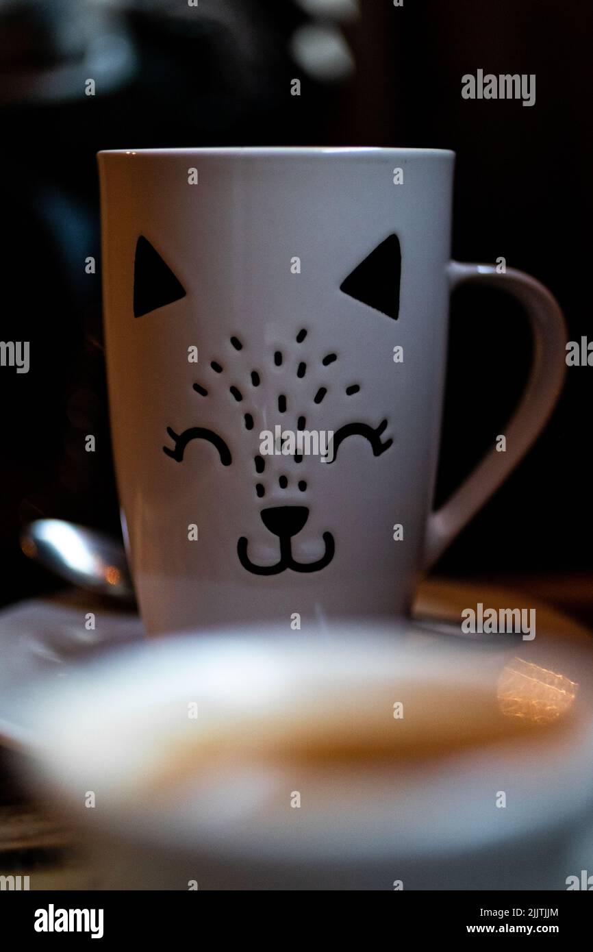 Une tasse blanche conçue avec un visage de chaton sur une table Banque D'Images