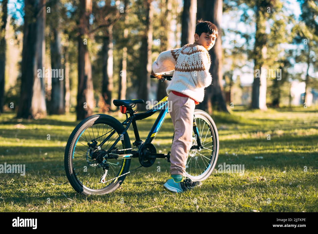 Un garçon caucasien en colère sérieux avec un vélo dans un parc par une journée ensoleillée Banque D'Images