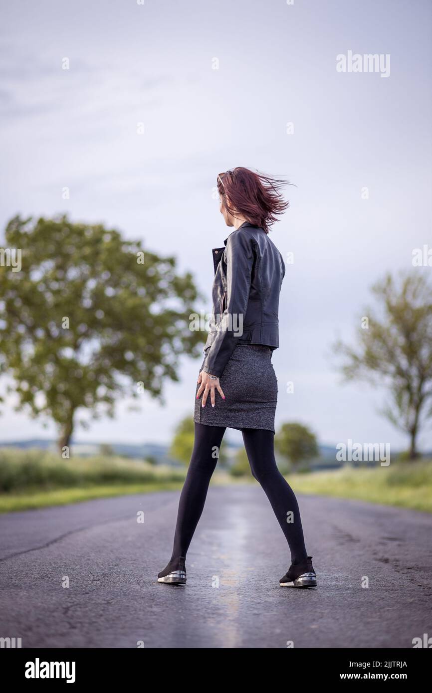 Une belle photo d'une jeune femme marchant sur une route traversant des champs verts par une journée ensoleillée Banque D'Images