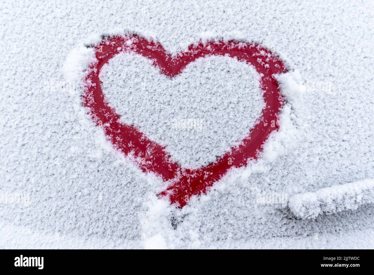 Coeur rouge neige sur la fenêtre de la voiture avec espace de copie. Coeur signe dans les flocons de neige frais. Symbole en forme de coeur dessiné sur le verre de voiture neigé. Concept d'amour. Valentin Banque D'Images