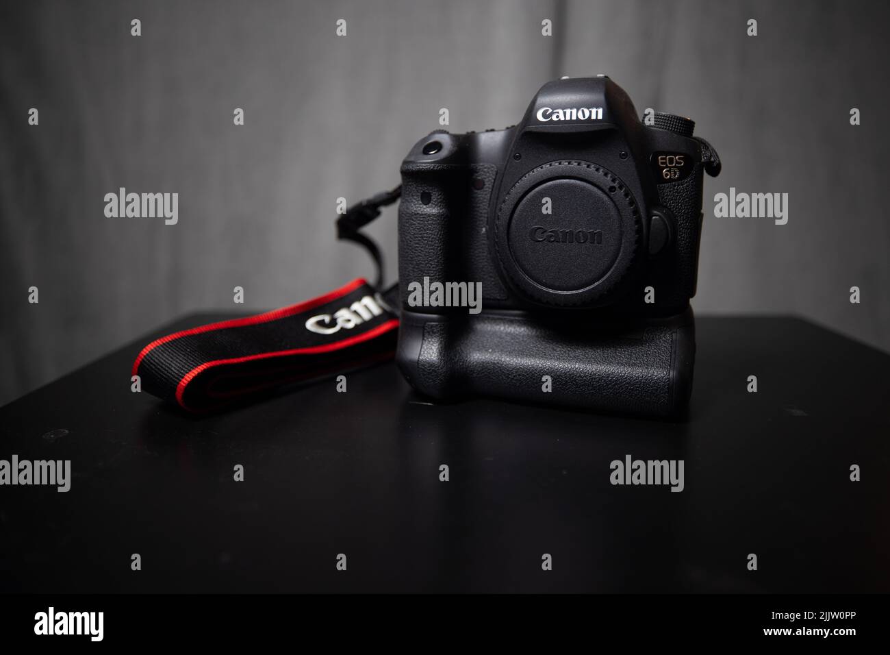 Un gros plan d'un appareil photo Canon 6D avec une poignée de batterie et une sangle sur un support noir isolé sur un fond gris Banque D'Images