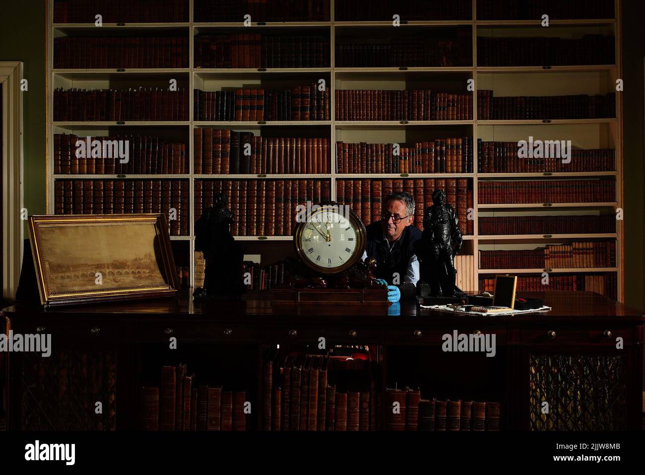 L'horologue Jonathan Betts inspecte une horloge en acajou Chippendale vers 1790, à l'intérieur de la bibliothèque de Stourhead House National Trust, dans le Wiltshire, où tous les anciens articles d'horlogerie exposés au public ont été liquidés pendant la pandémie et sont maintenant en cours de service, de blessure et de vérification, ainsi, ils peuvent à nouveau marquer et sonner en tant que chronométreurs fonctionnels et historiques. Date de la photo: Jeudi 28 juillet 2022. Banque D'Images