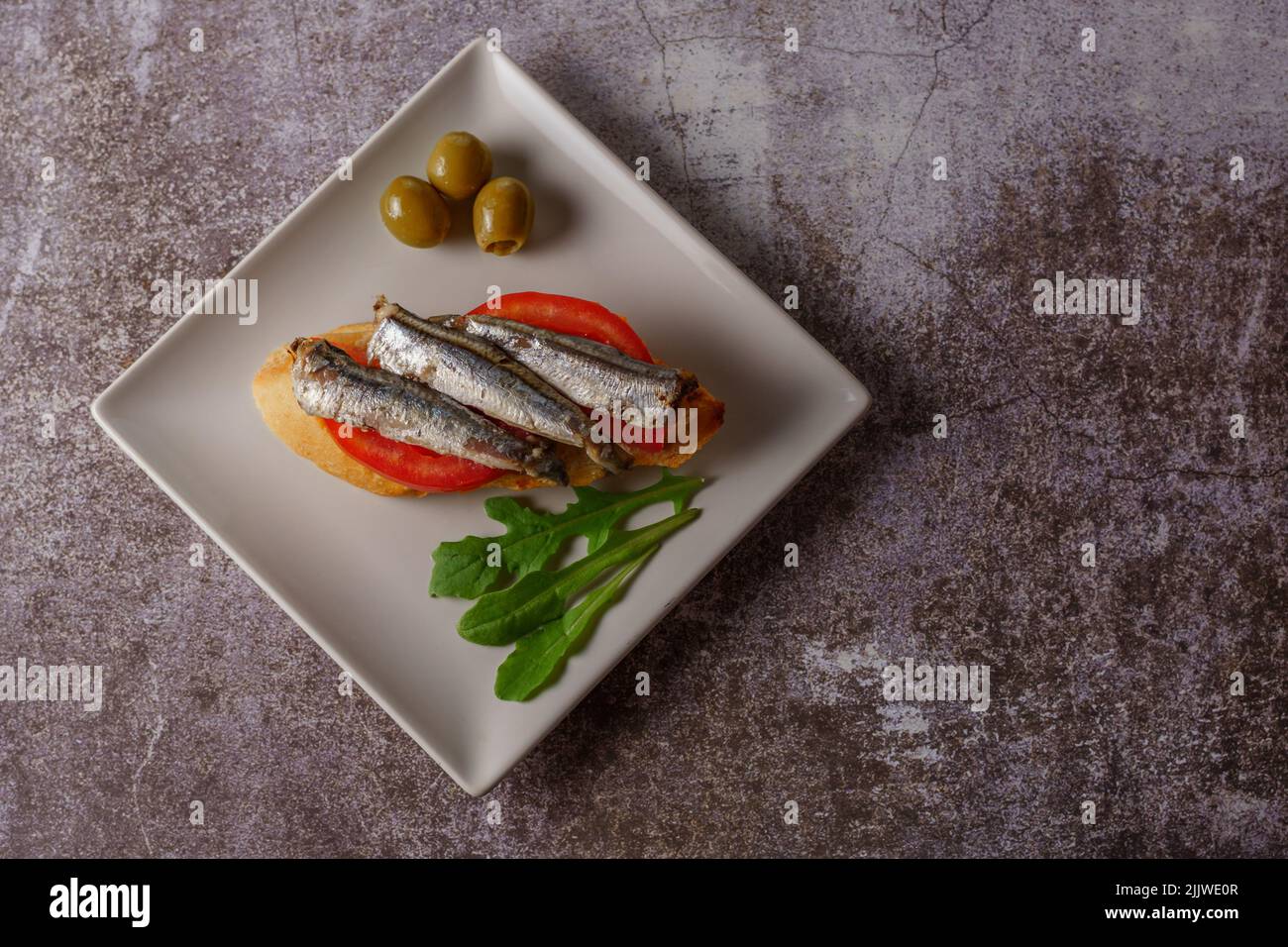 tapa de sardines sur une tranche de pain à la tomate et aux olives sur une assiette blanche avec un fond blanc typiquement espagnol Banque D'Images