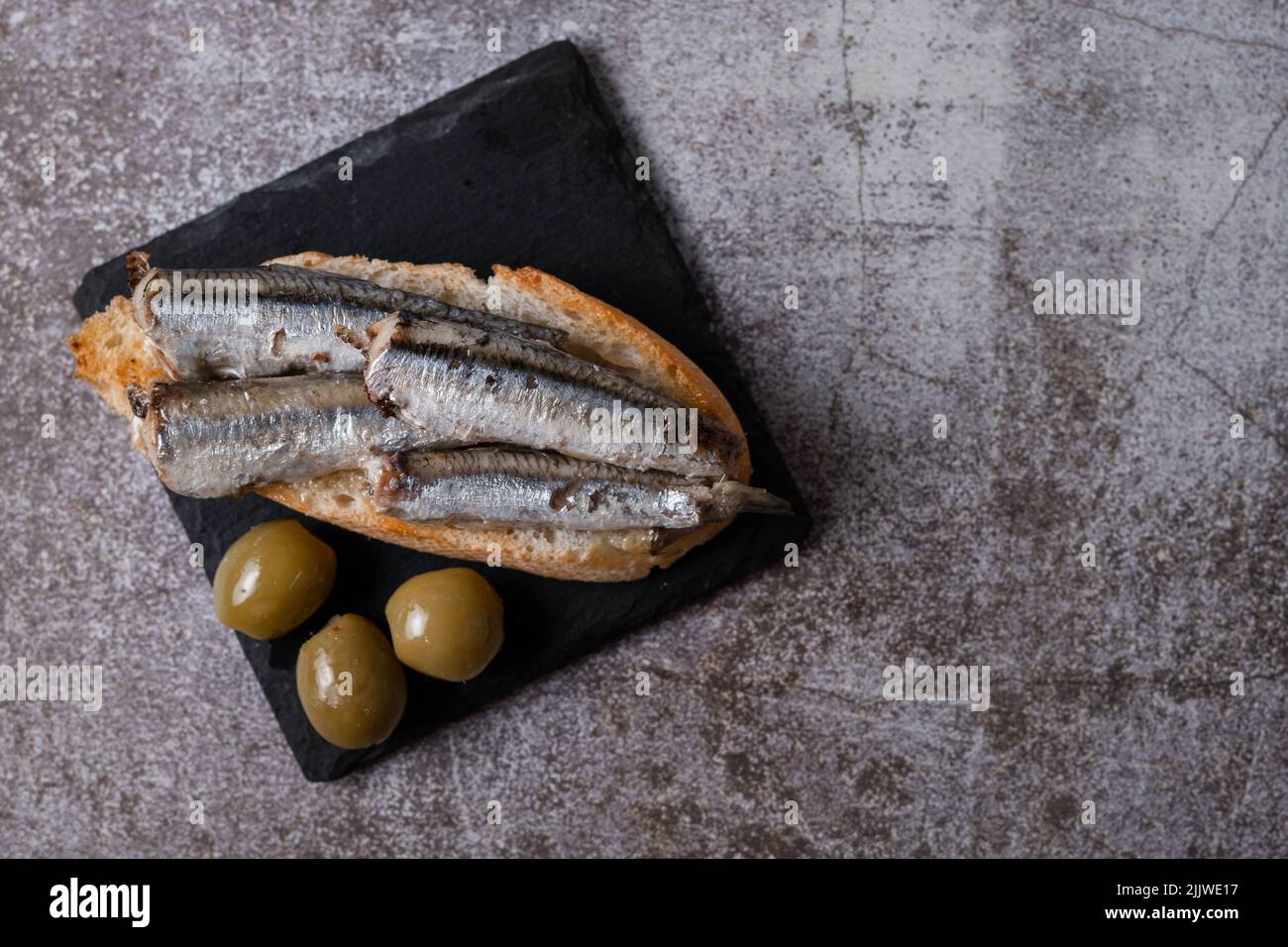 Tapa de sardines sur une tranche de pain avec tomate et olives sur ardoise noire typique espagnol Banque D'Images