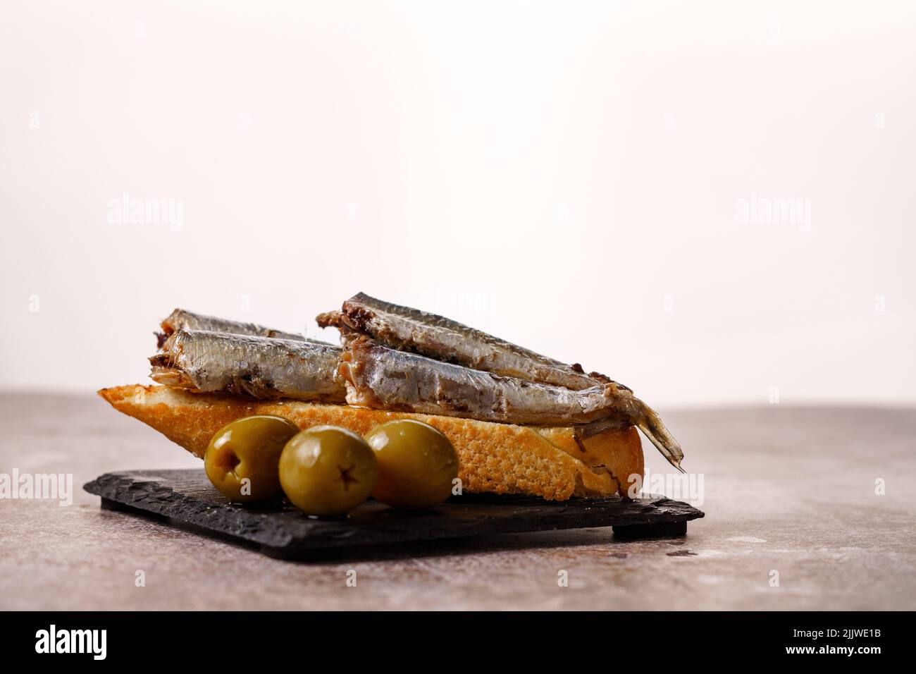 Tapa de sardines à la tomate et aux olives sur ardoise noire et fond blanc typiquement espagnol Banque D'Images