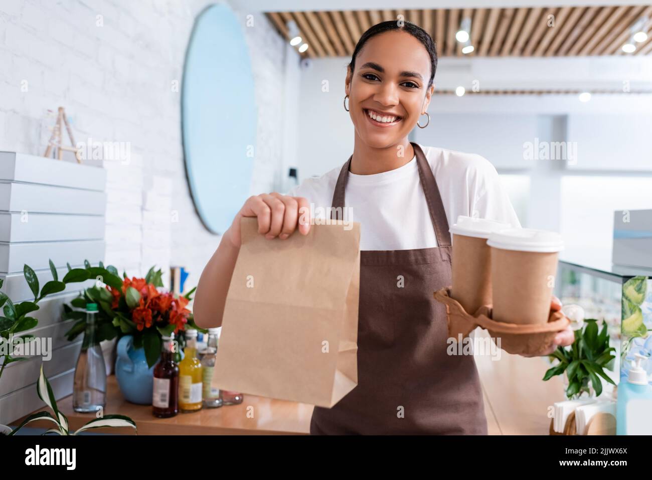 Vendeur afro-américain positif tenant le café à emporter et sac de papier dans la sucrée Banque D'Images