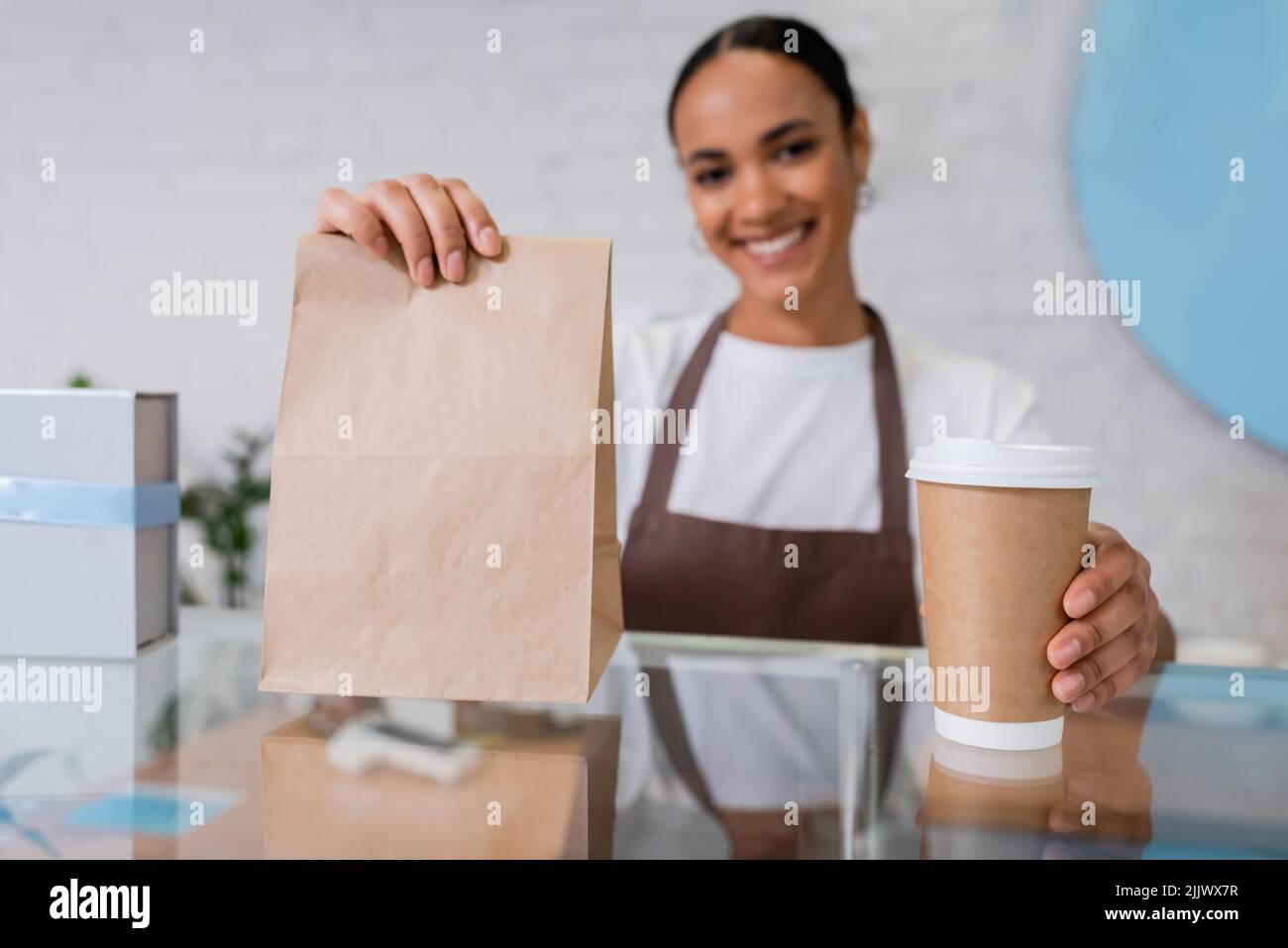 Café à emporter et sac en papier entre les mains d'un vendeur afro-américain flou dans un magasin de sucreries Banque D'Images