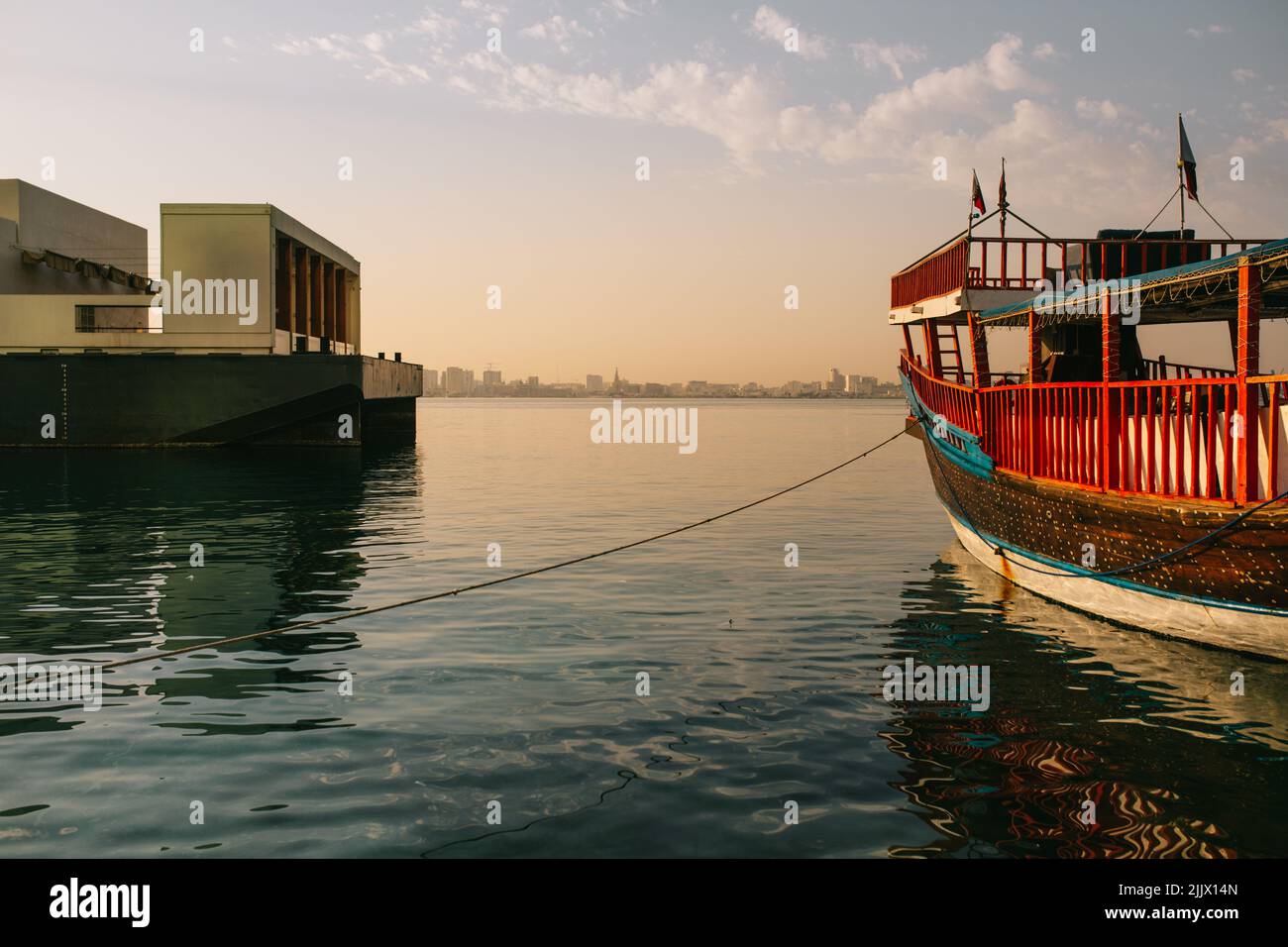 Bateau traditionnel attaché à la jetée avec corde flottant sur l'eau de mer ondulée contre ciel bleu nuageux au coucher du soleil à Doha, Qatar Banque D'Images