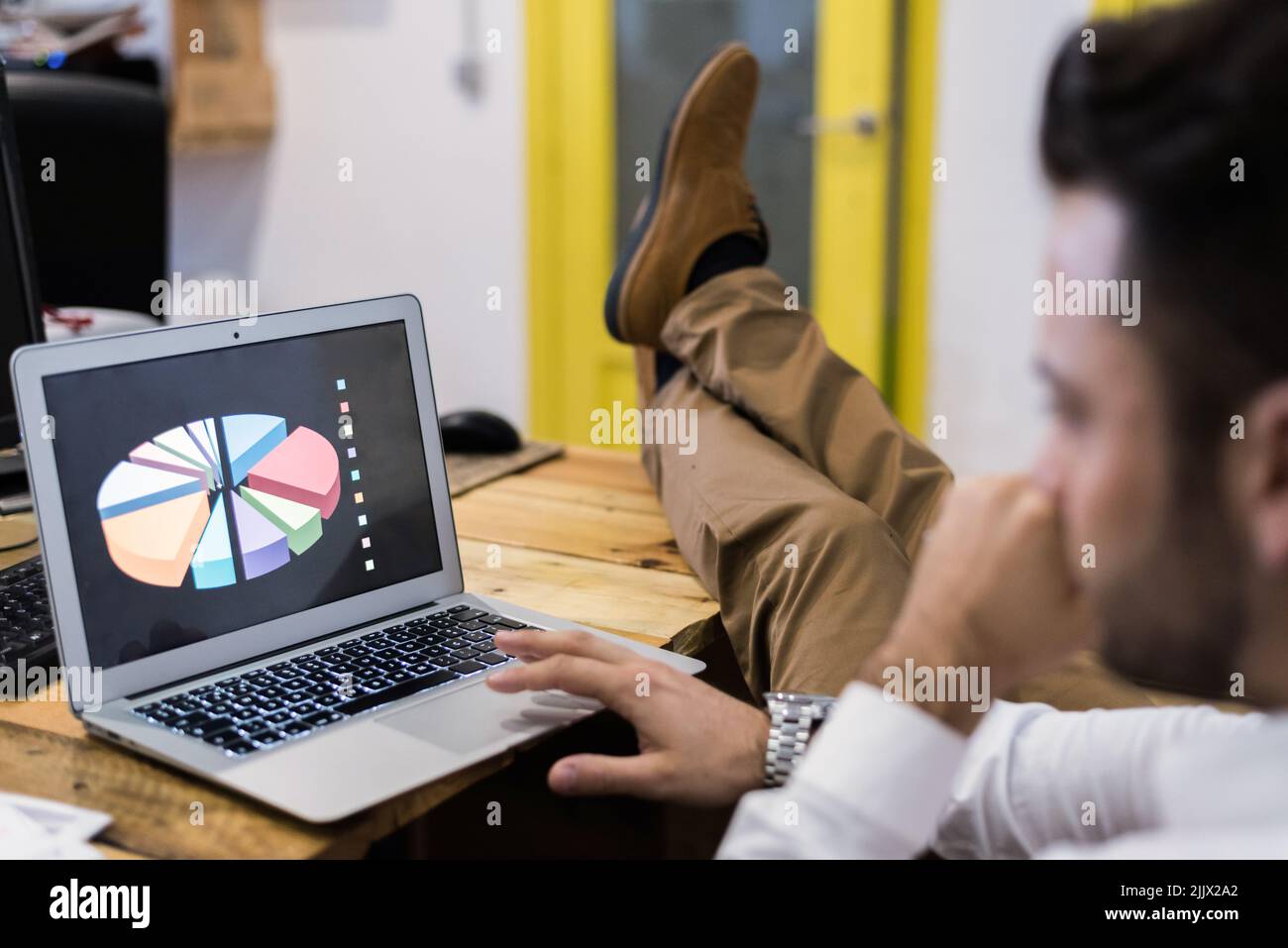 Vue latérale d'un travailleur de culture ciblé parcourant un netbook avec des graphiques tout en travaillant sur un projet professionnel dans un espace de travail moderne et léger Banque D'Images