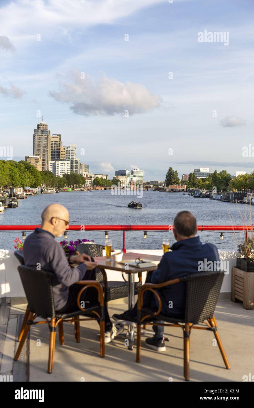 2022-07-27 20:15:52 AMSTERDAM - de la terrasse du pavillon du Royal Amsterdam Roei- en Zeilvereeniging de Hoop, vous pouvez regarder par-dessus l'Amstel avec une bière. Fondé en 1848, de Hoop est le plus ancien club sportif d'Amsterdam et le deuxième plus ancien club hollandais d'aviron et de voile. Le pavillon avec le club est une apparence frappante sur le côté Weesper de l'Amstel qui serpente à travers la capitale. ANP NILLA BERRETTY-VAN LOENEN pays-bas sortie - belgique sortie Banque D'Images