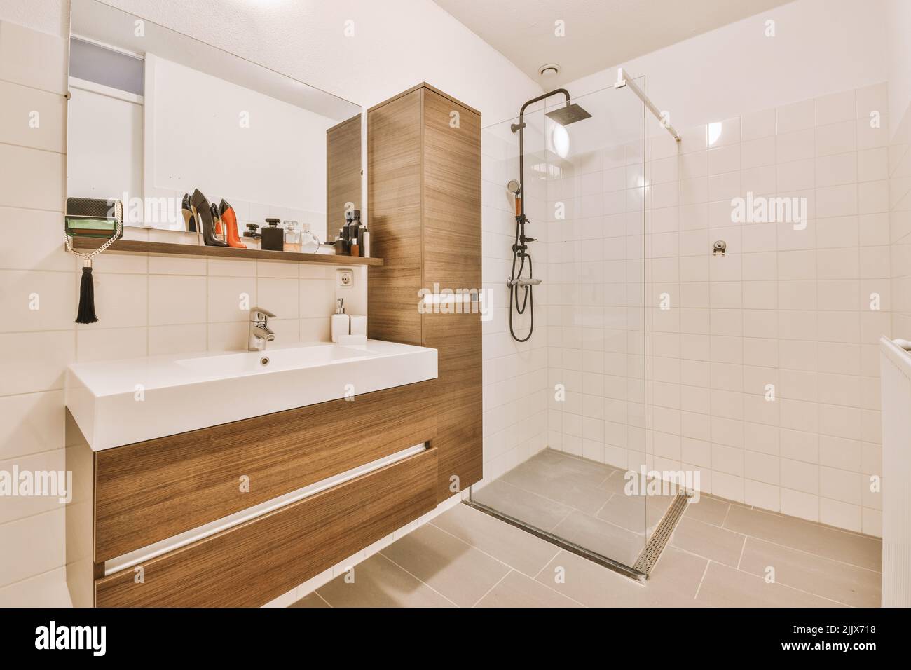 Mobilier en bois et grand miroir dans la salle de bains moderne et spacieuse avec douche et mur carrelé dans la maison moderne Banque D'Images