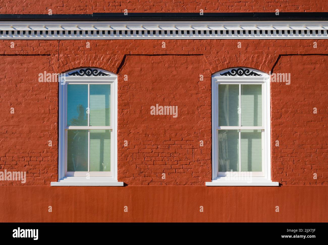 Deux fenêtres encadrées de blanc dans un bâtiment en brique rouge de couleur riche avec scrollwork et cornice avec un groupe de briques au fond Banque D'Images