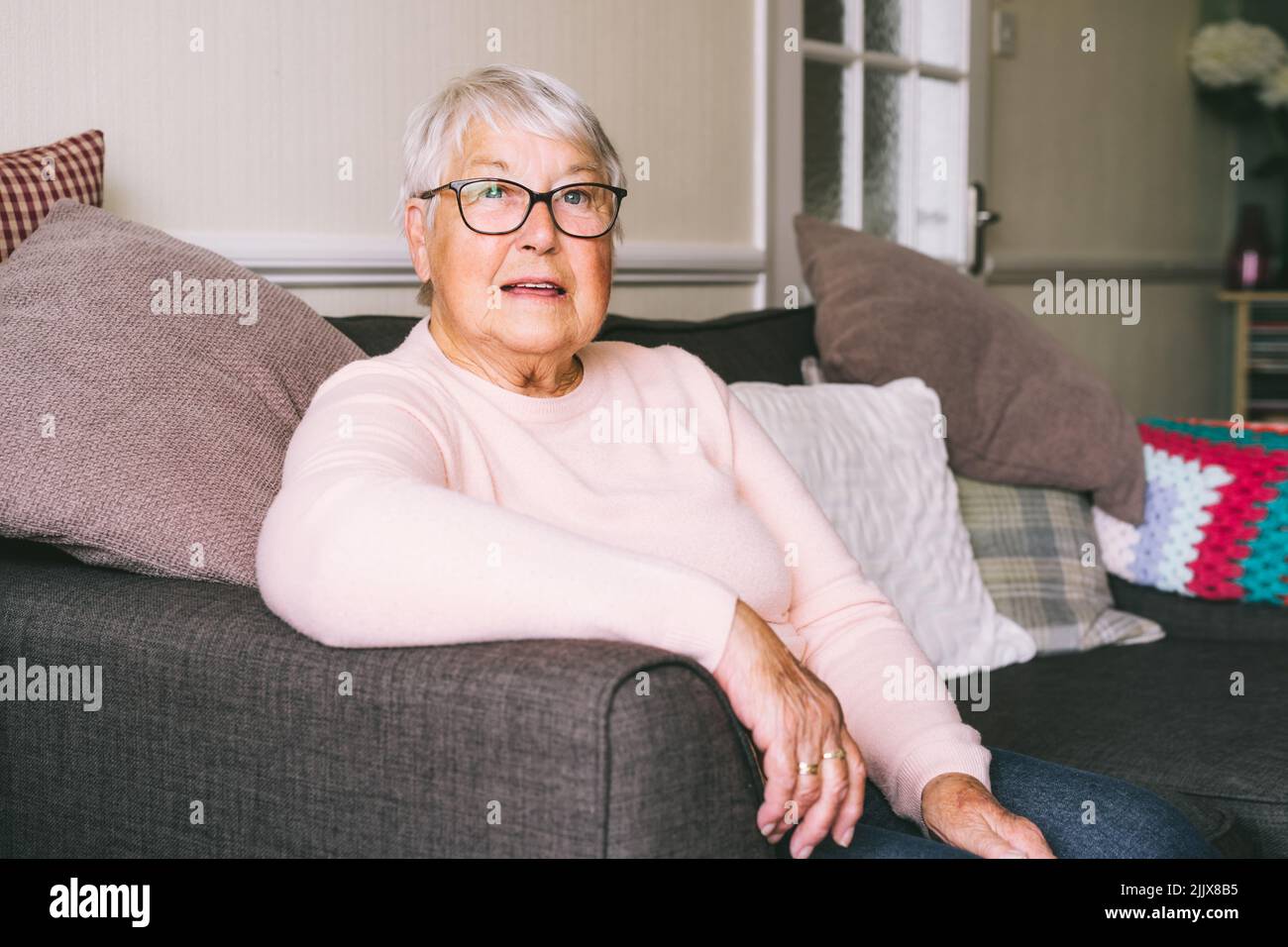 Portrait d'une grand-mère à la retraite, mûre et souriante, en lunettes, femme âgée souriant assise sur un canapé à la maison, profitant de la retraite. Foc sélectif Banque D'Images Portrait d'une grand-mère à la retraite, mûre et souriante, en lunettes, femme âgée souriant assise sur un canapé à la maison, profitant de la retraite. Foc sélectif Banque D'Images