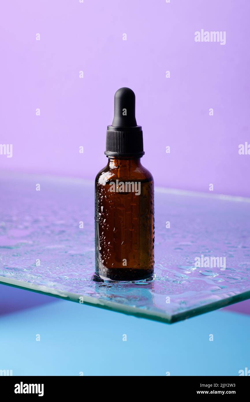 Bouteille de produit cosmétique, verre foncé avec pipette sur étagère en verre, fond violet, regarder vers le haut Banque D'Images