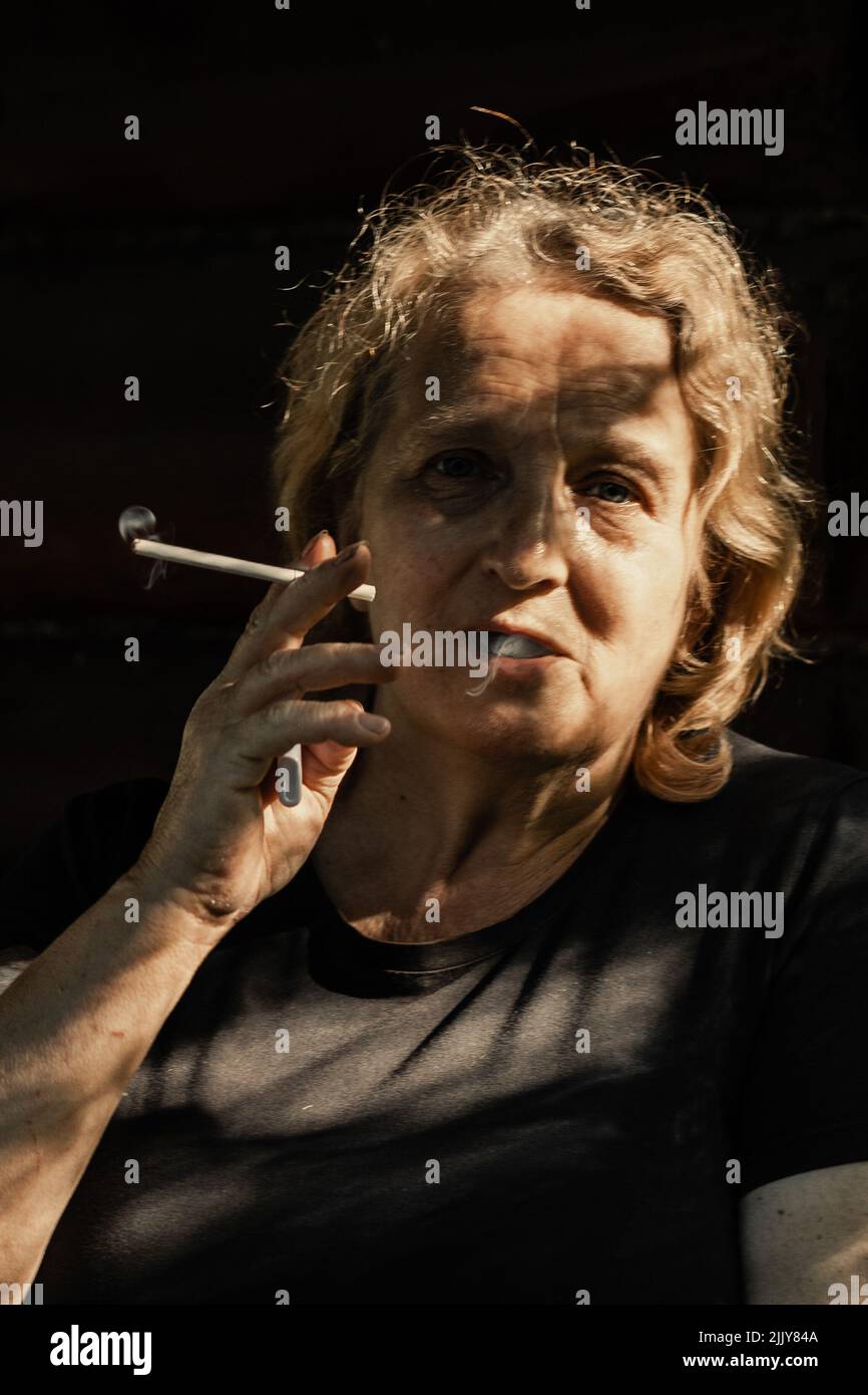 Portrait d'une femme âgée avec une cigarette en gros plan sur un fond naturel. Lumière du coucher du soleil sur le visage de l'aîné. Photo de haute qualité Banque D'Images