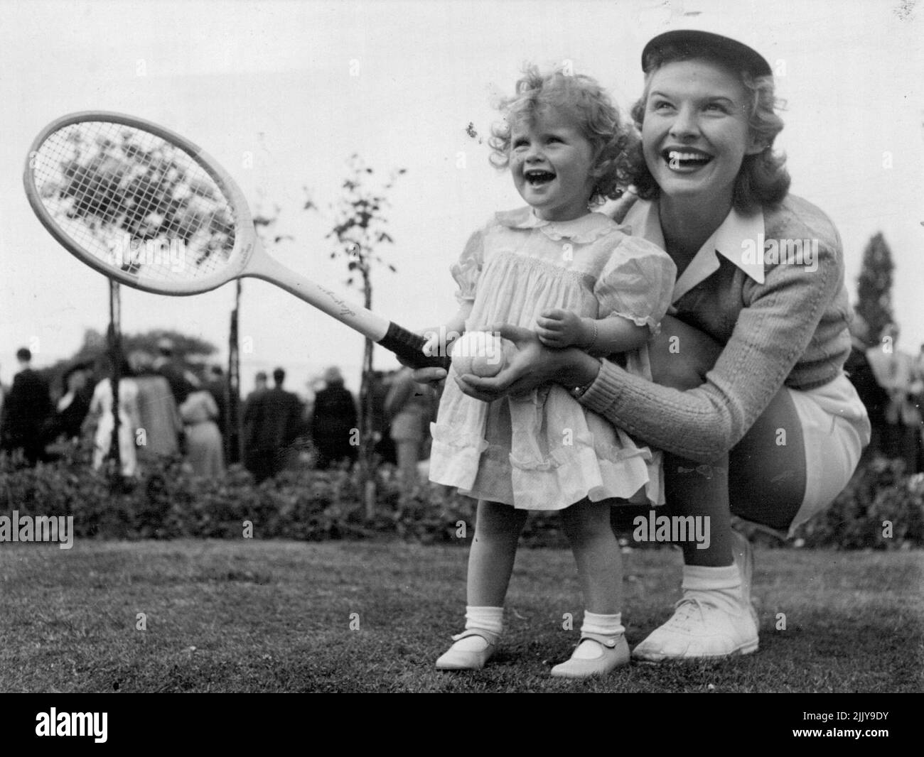 Joy montre son service - Auntie Joy obtient un conseil, sur la façon de servir un «as» ***** Son neice, Joy Panton, âgée de vingt mois, pendant une ***** Pour les joueurs du tournoi de Wimbledon qui se tiendra hier au Burlingham Club, Londres. Auntie Joy - Mme Mottram, épouse du joueur de la coupe Davis britannique Tony - était un simple gilet, une chemise unie et des shorts ordinaires pour les jeux de knockup qui ont été joués pendant la réception. 25 juin 1951. (Photo par Daily Mirror). Banque D'Images