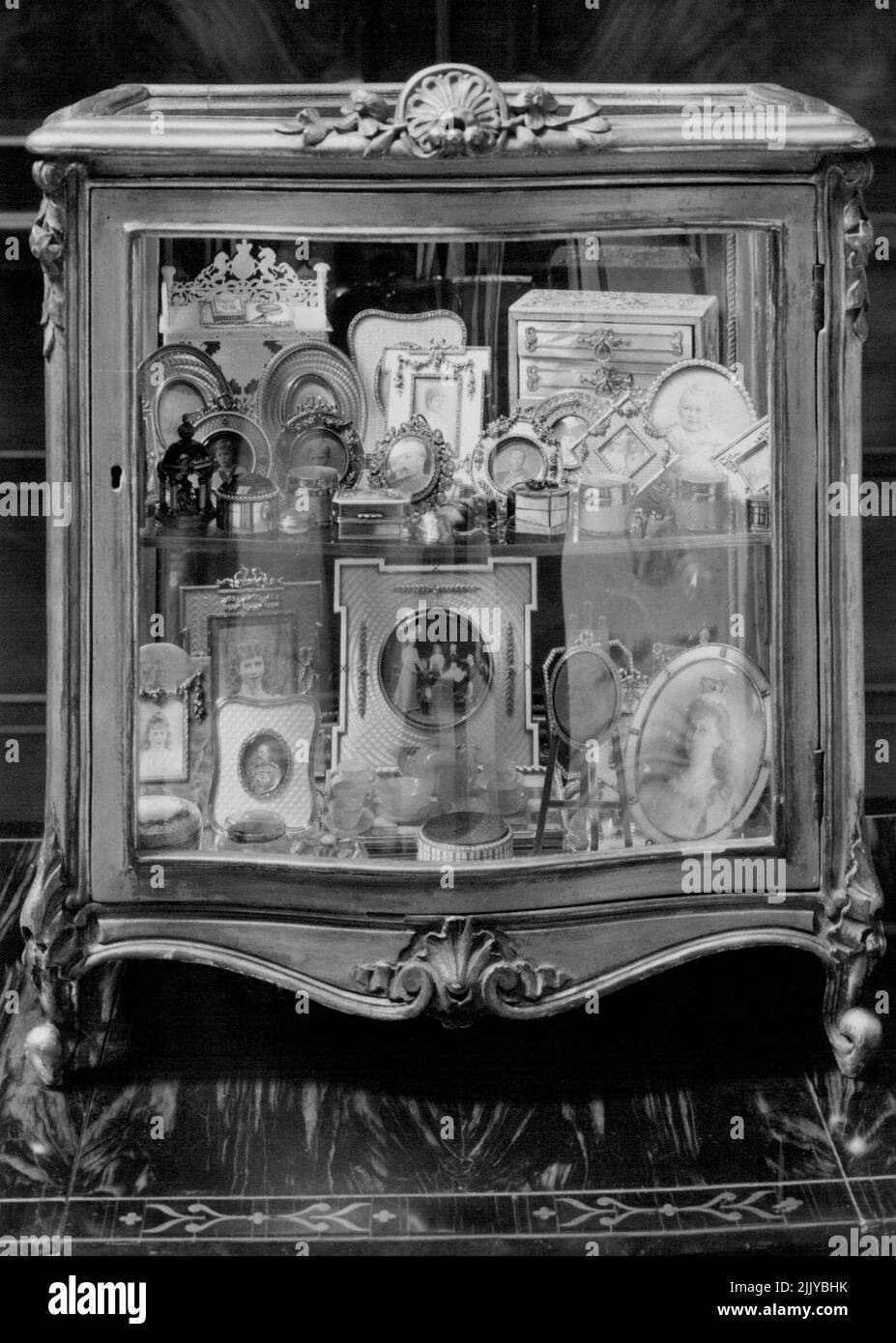 Est cas sont divers bibelots, principalement associés à divers membres de la famille royale, y compris des miniatures et de petites photographies dans des cadres de bijoux du roi Edouard VII, la reine Alexandra, le roi George V, la reine Mary, etc; Une commode miniature en nacre montée d'or; un bureau de lecture miniature de service de nacre sur un plateau et un portrait camée du duc de Windsor dans un ovale de diamants et d'or, sur un chevalet doré, Qui a été donné à la reine Marie par le roi George V, à l'occasion de l'investiture du duc en tant que prince de Galles en 1912. 26 mai 1954. (Photo de Fox photos). Banque D'Images