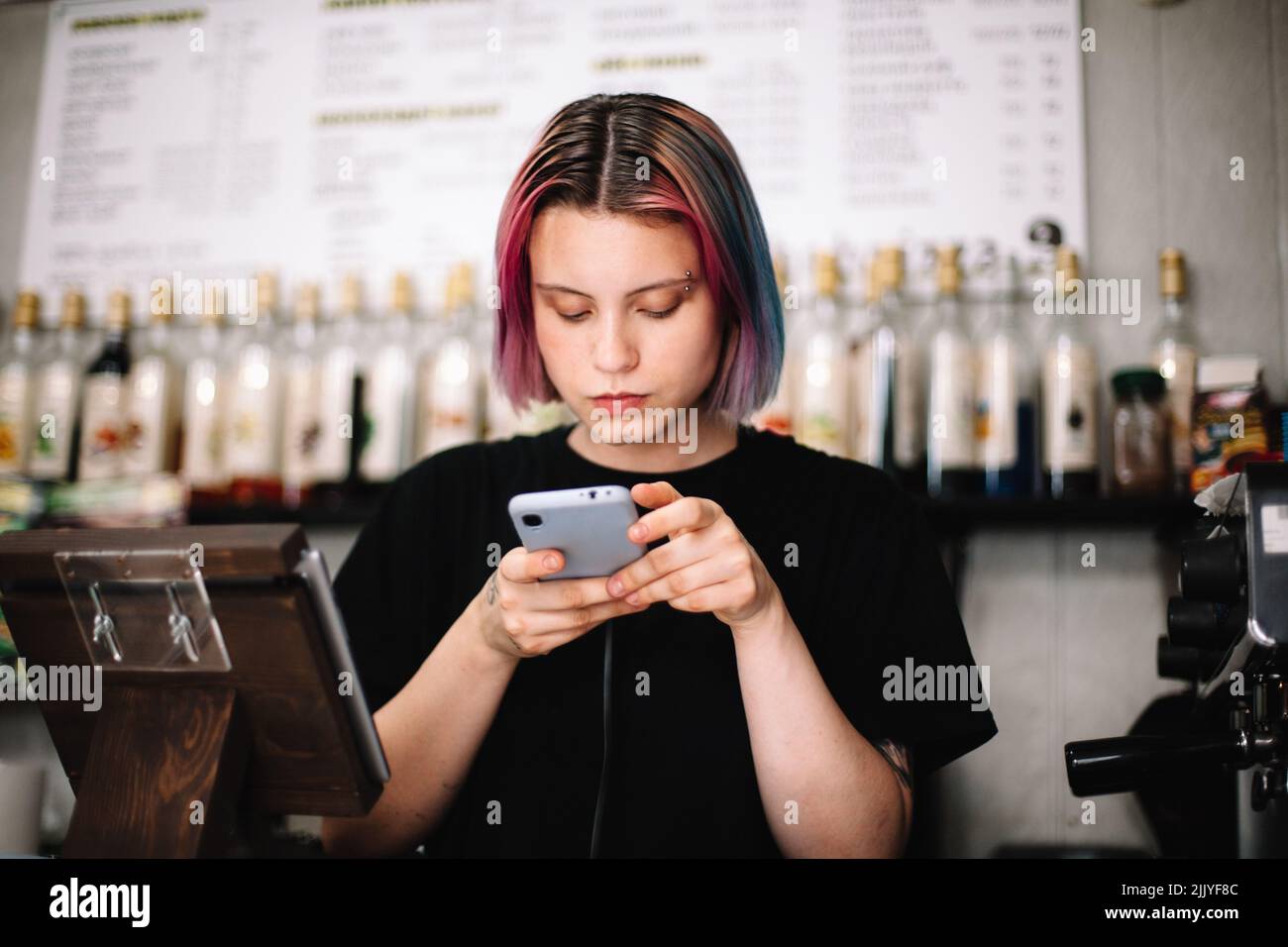 Femme Barista utilisant un smartphone au comptoir de caisse du café Banque D'Images