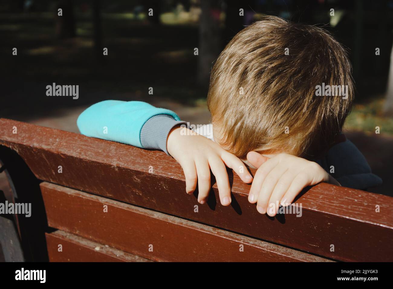 Triste garçon cache son visage derrière un banc de parc à l'extérieur de près Banque D'Images