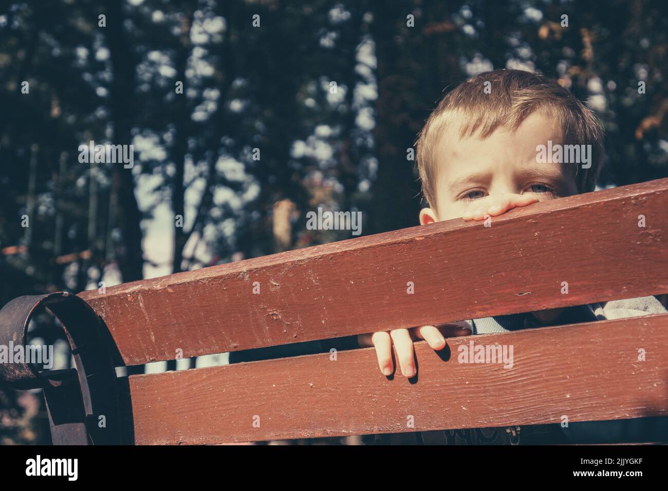 Triste garçon cache son visage derrière un banc en bois dans le parc Banque D'Images