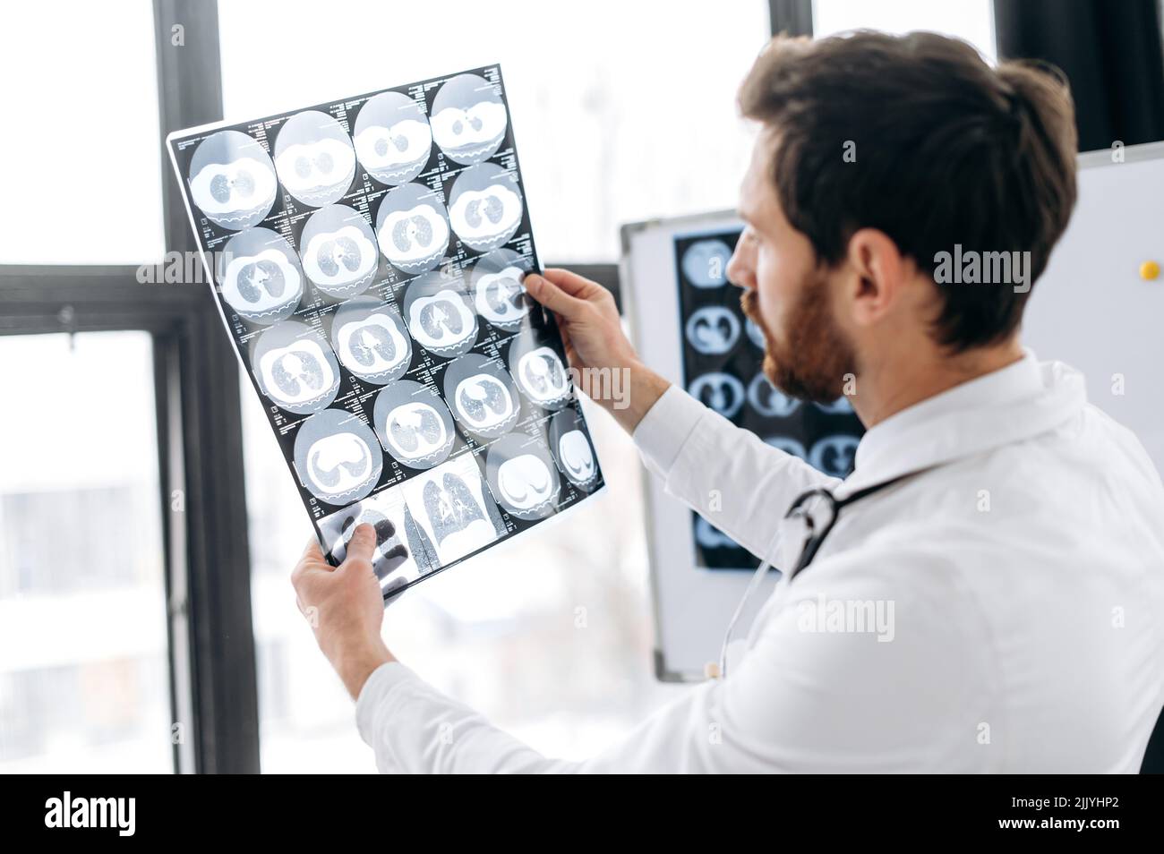 Médecin professionnel regardant la radiographie à son cabinet, thérapeute mâle caucasien en uniforme médical blanc et des lunettes concentré d'apprentissage de la radiographie du patient, debout dans son bureau médical Banque D'Images