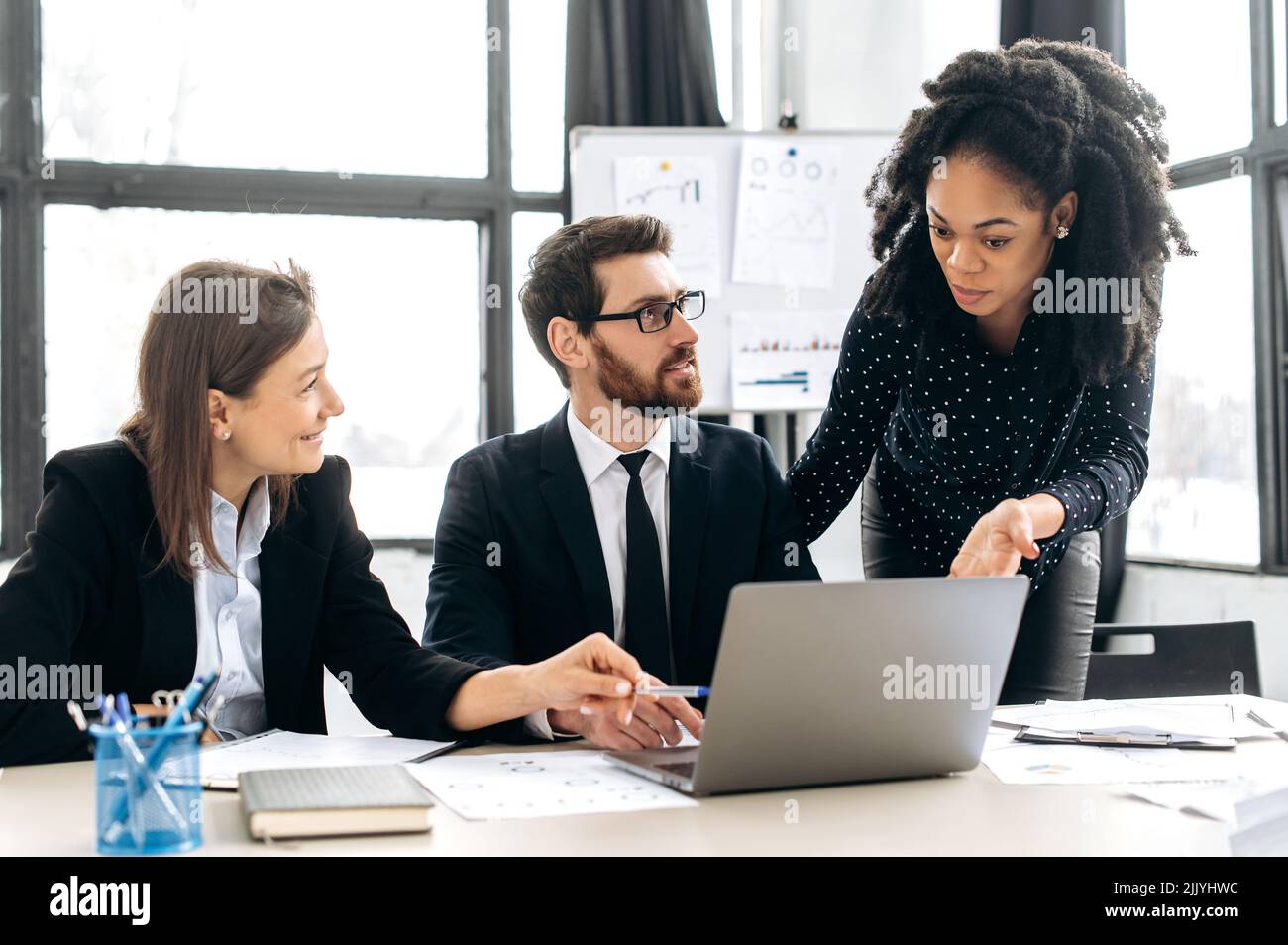 Les collègues multiraciaux font des brainstorming sur la stratégie ensemble, assis dans un bureau créatif moderne, étudiant des documents, utilisant un ordinateur portable, discutant. Collaboration d'équipe de professionnels Banque D'Images