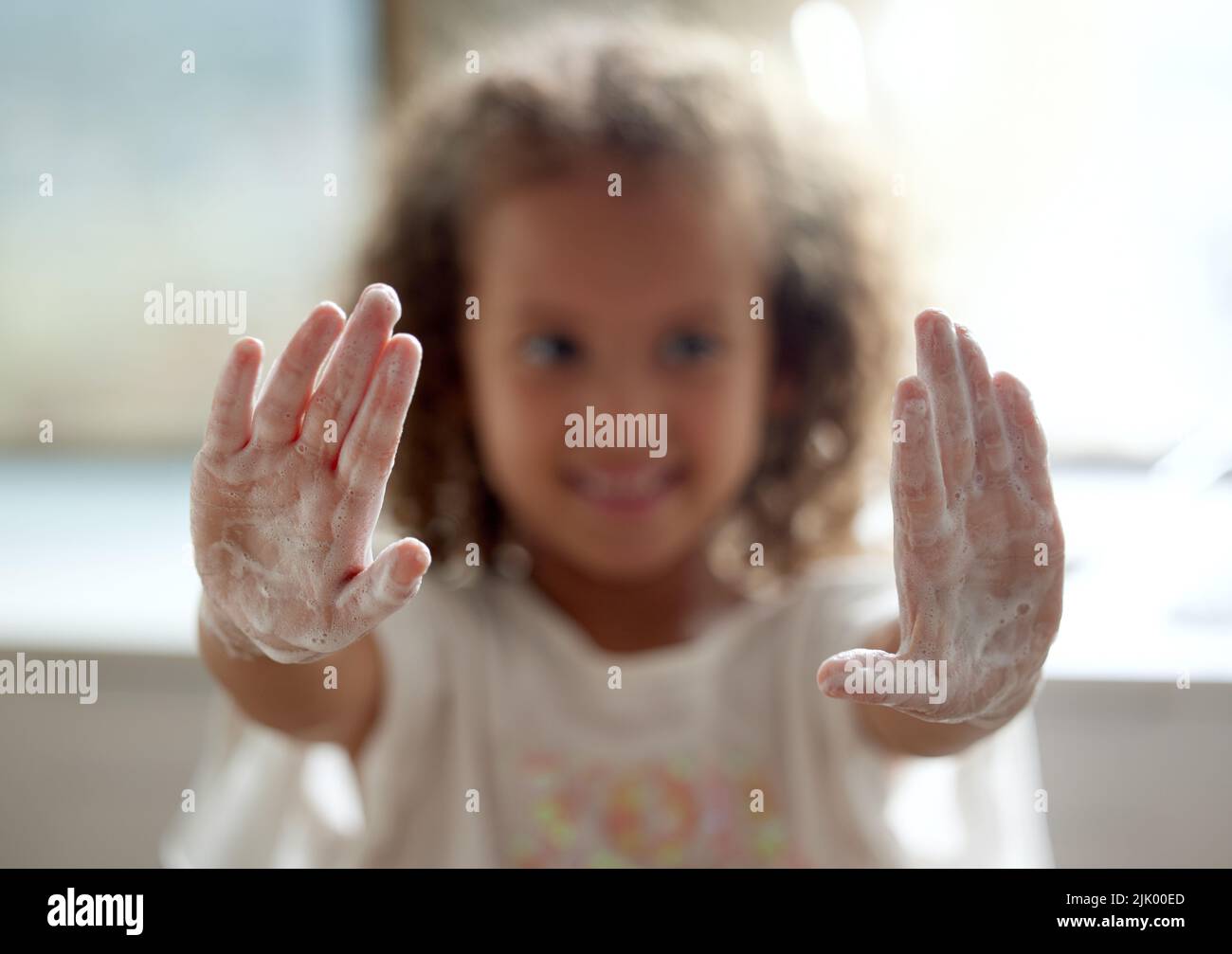Nettoyer, hygiène et protection contre les infections par une petite fille se lavant les mains avec du savon moussant. Portrait d'un enfant montrant des paumes savonneces avec un désinfectant pour Banque D'Images
