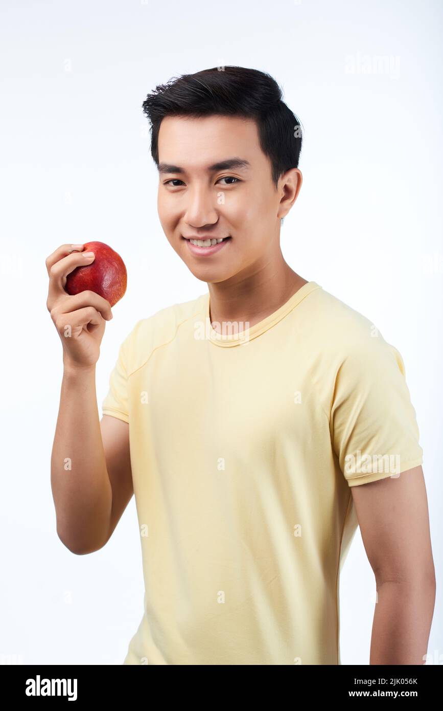 Portrait à la taille de l'homme asiatique gai regardant l'appareil photo avec un sourire éclatant tout en tenant la pomme rouge fraîche à la main, isolée sur fond blanc Banque D'Images