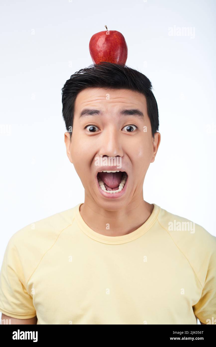 Portrait d'un homme asiatique effrayé avec une pomme rouge sur la tête, regardant l'appareil photo et criant au sommet de la voix, isolé sur fond blanc Banque D'Images